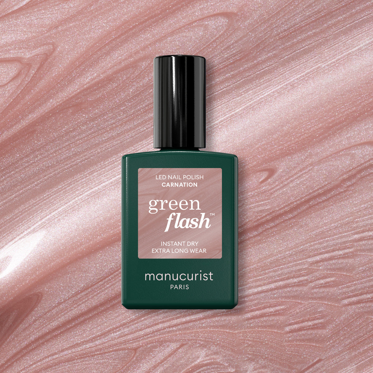 A green Manucurist Green Flash gel polish bottle in the shade Carnation sits on a shimmery pink surface that echoes the shimmer of the Carnation shade.