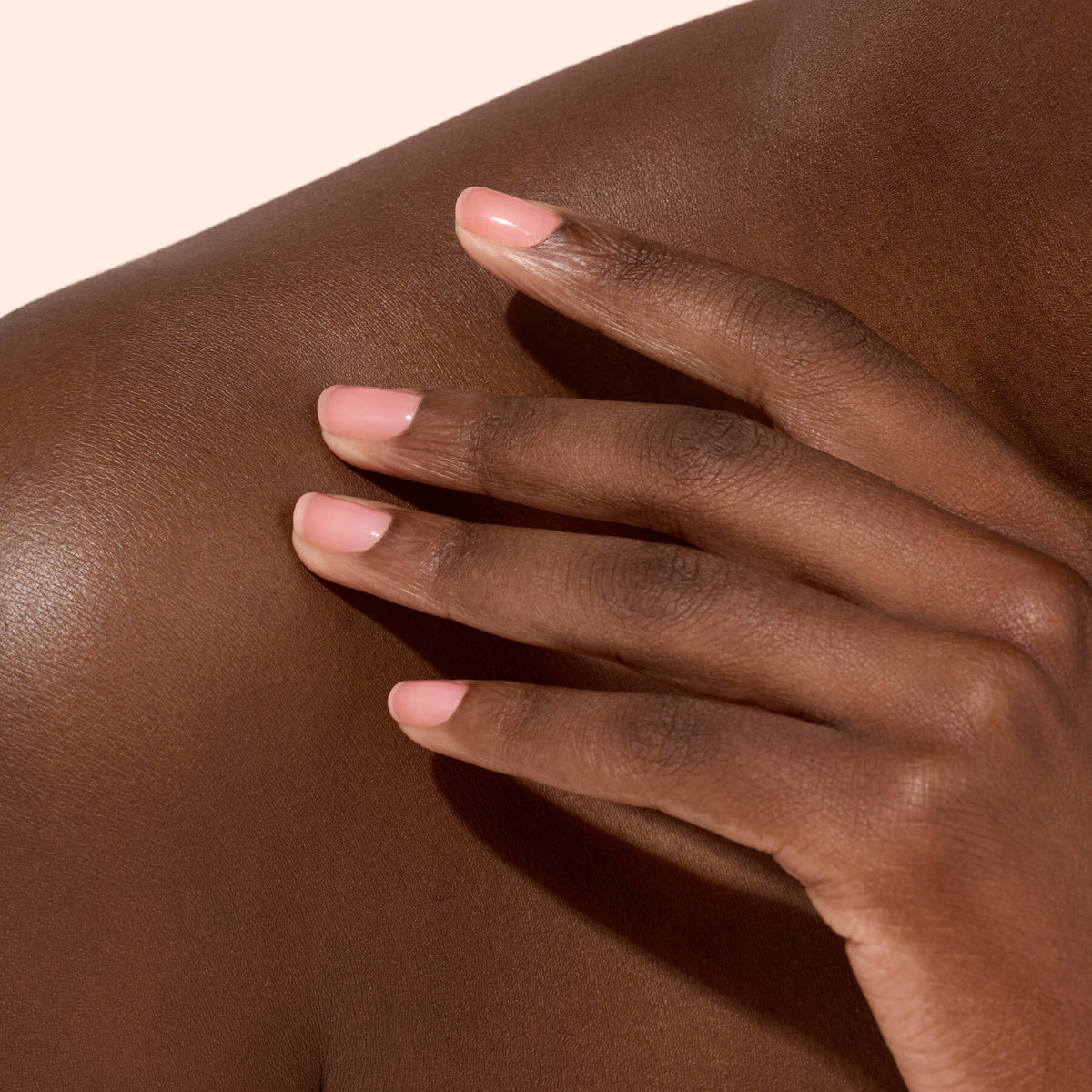 A close-up of a hand with natural, neatly manicured nails—highlighting the benefits of Manucurist’s Active™ Glow Cranberry—resting gently on a person’s bare shoulder against a neutral background.