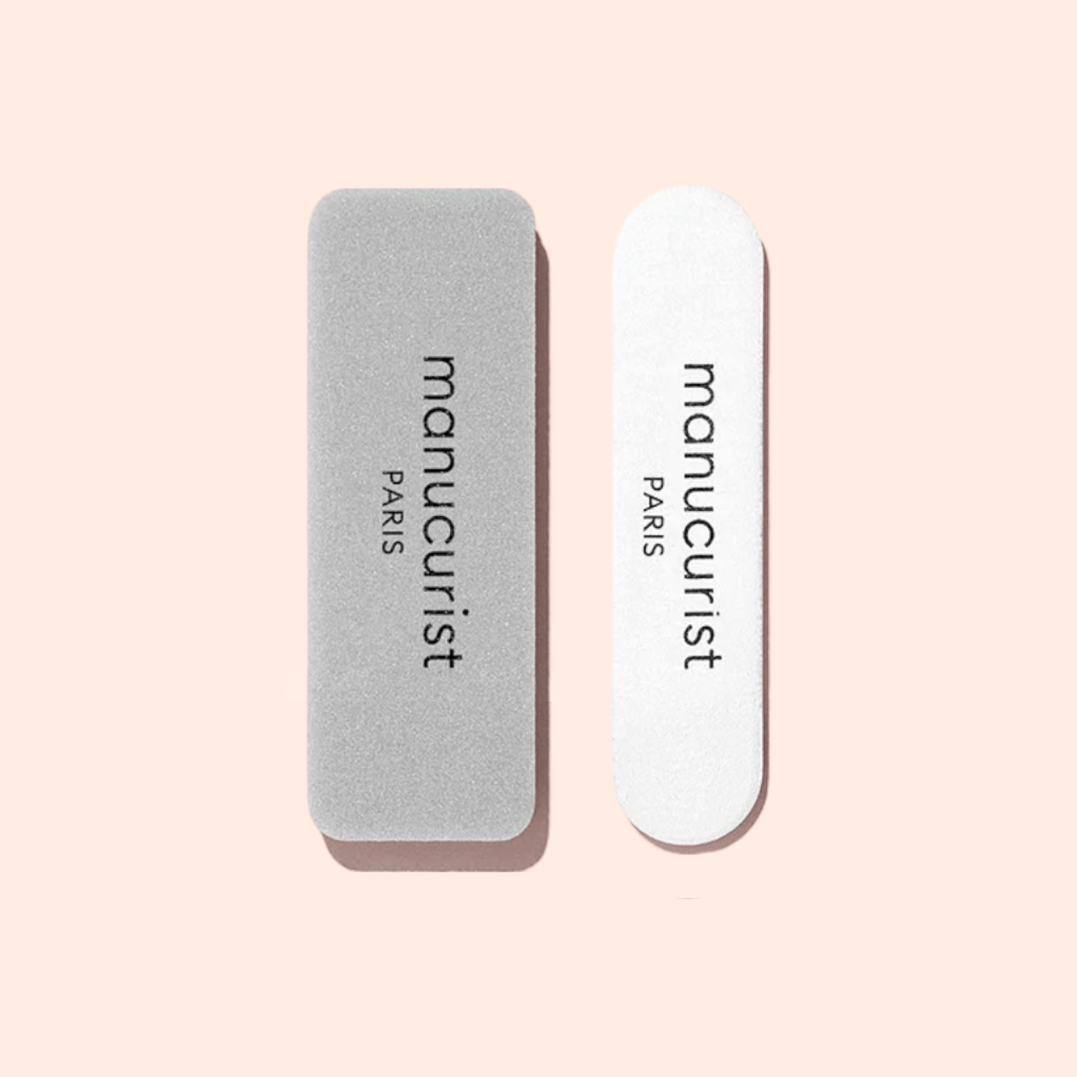 The Manucurist-test Mini Nail File Duo - Free, featuring a rectangular grey nail buffer and a white rounded nail file, is displayed on a pale pink background.