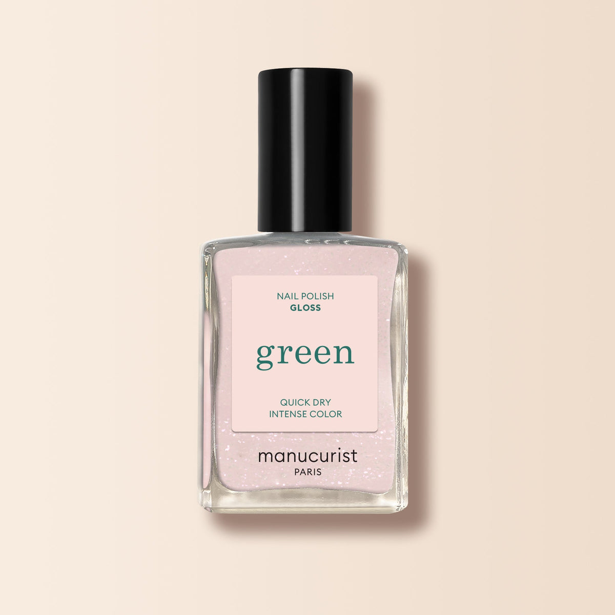 A bottle of Manucurist Gloss nail polish with a black cap contains pale pink, iridescent shimmer polish. The label reads: “Nail Polish Gloss, Green, Quick Dry Intense Color.” Set against a light beige background.