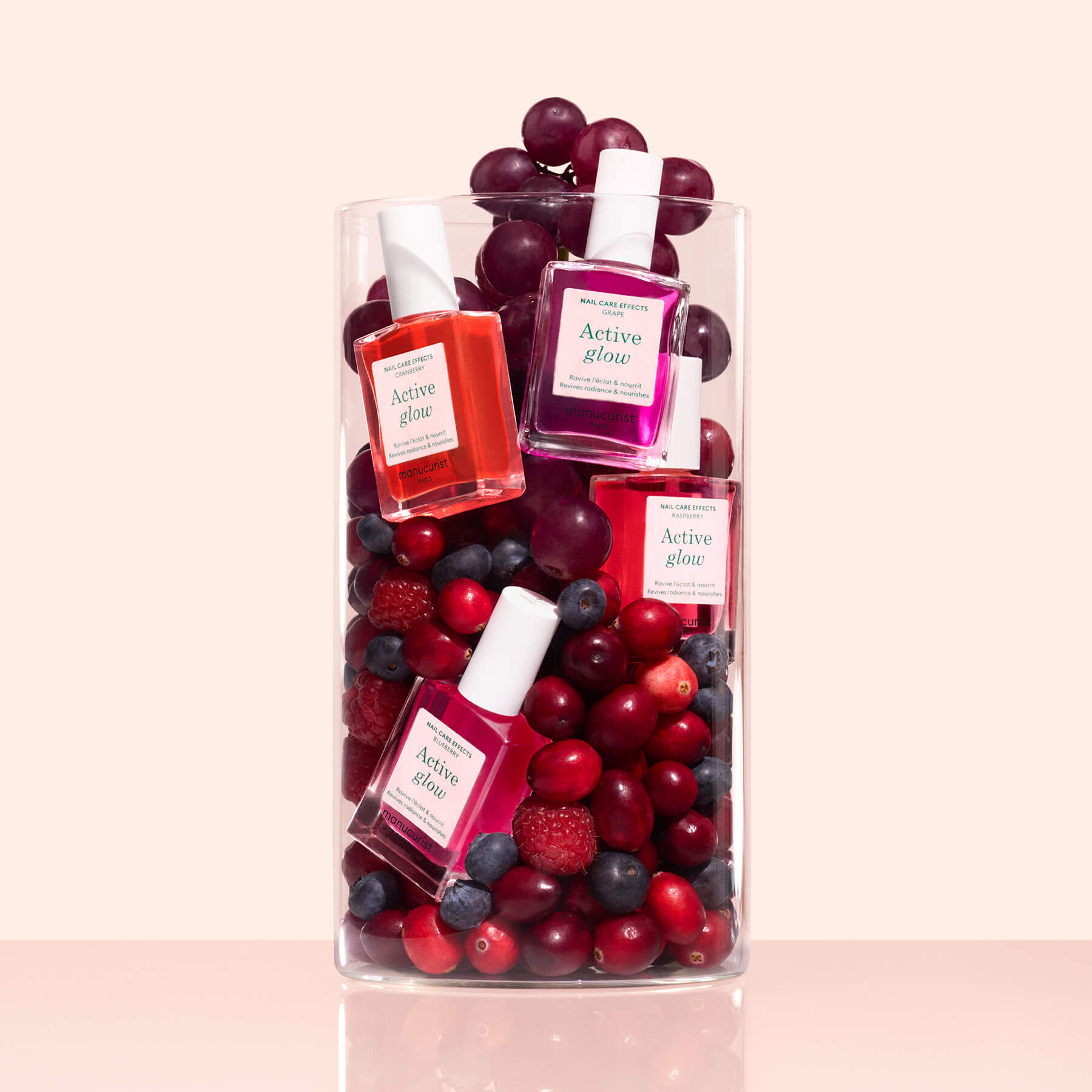 A clear glass vase with red grapes, cranberries, blueberries, and raspberries holds Manucurist&