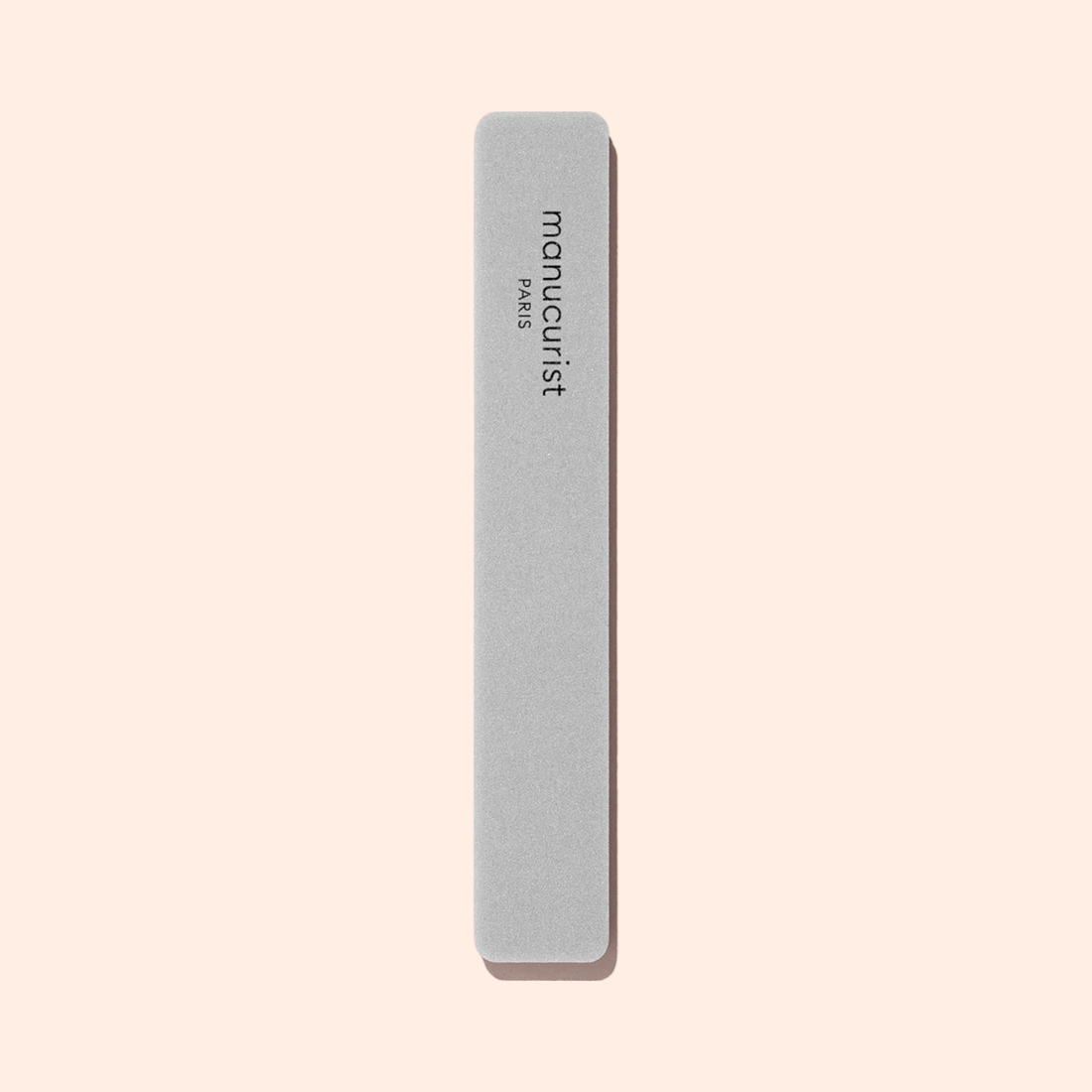 A light gray Nail buffer sponge by Manucurist, rectangular with rounded edges and “manucurist PARIS” printed vertically, is shown on a plain beige background.