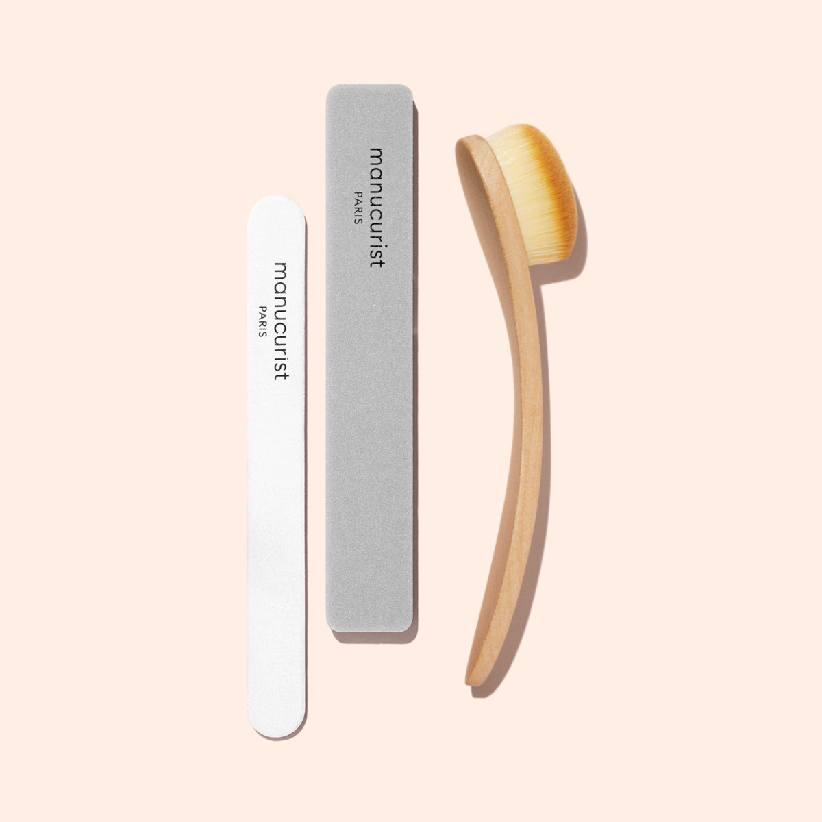 The Manucurist Dust Brush with vegan bristles, a gray buffer, and a white nail file labeled "manucurist PARIS" are arranged on a light beige background, ready to perfect your nails.