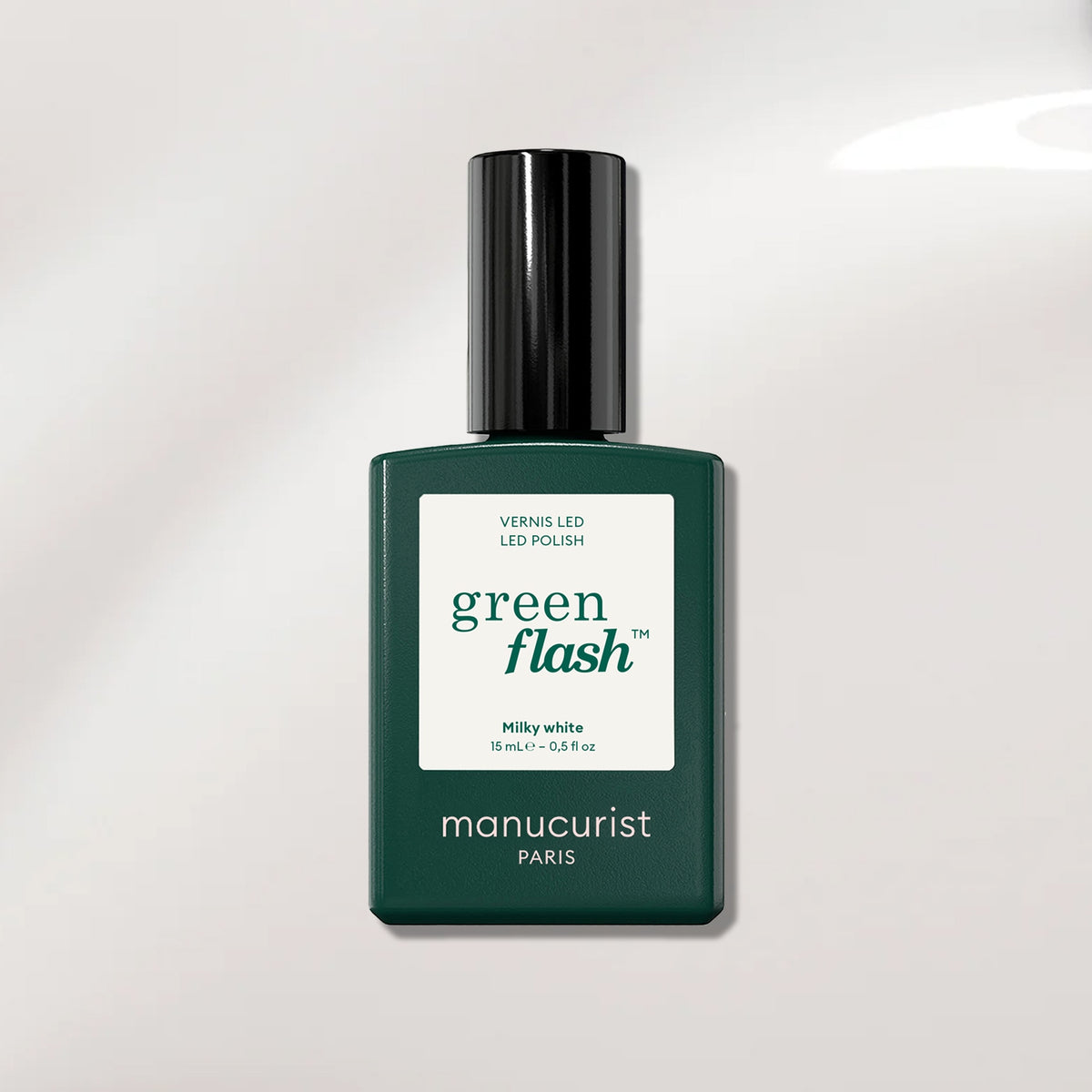 A bottle of Manucurist Milky White gel polish with a dark green rectangular base, black cap, and white label sits on a light surface. This polish gives nails a clean, luminous milky white finish.