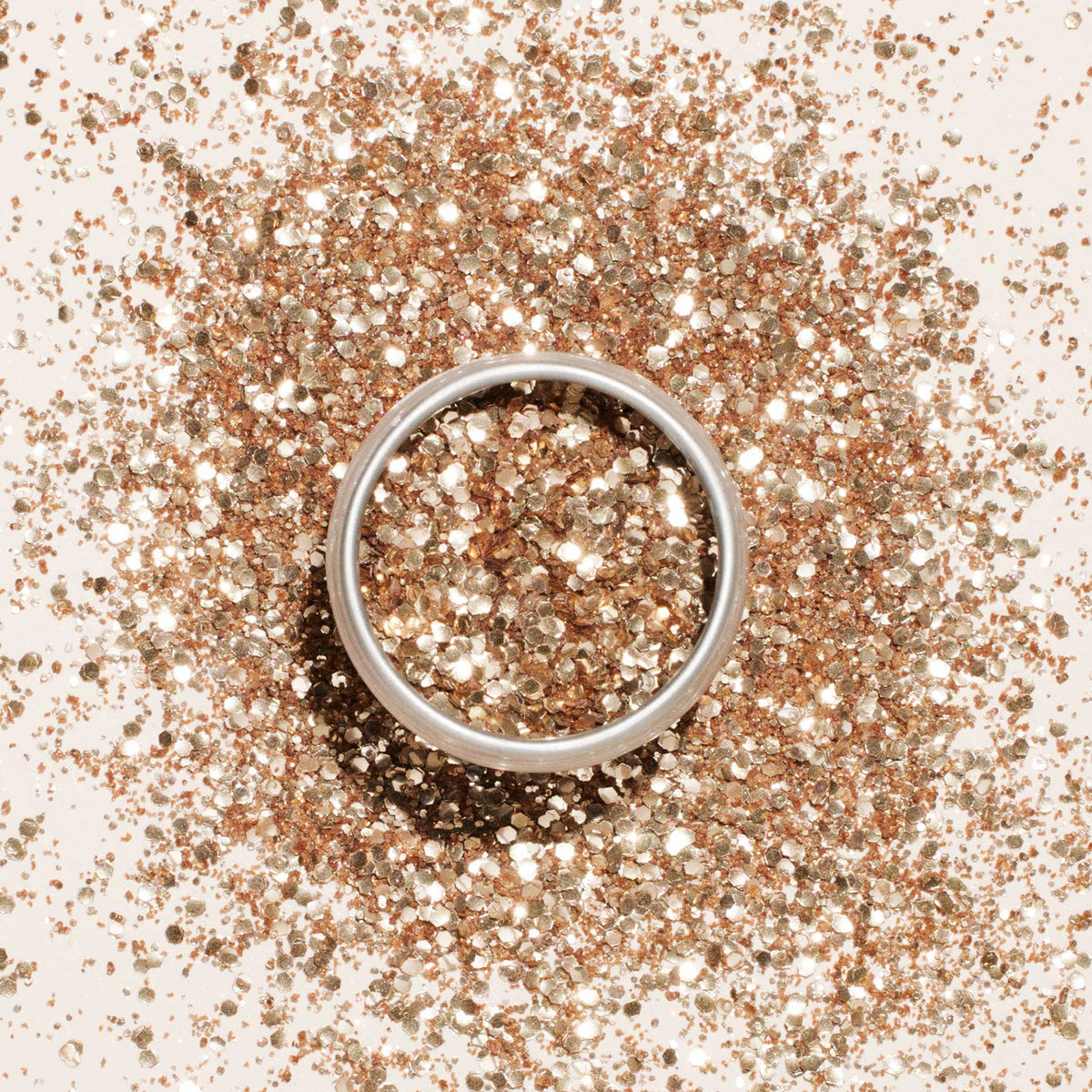 A silver ring rests on a surface sprinkled with Manucurist Biodegradable glitter, which fills and surrounds the ring, creating a sparkling, festive effect as the eco-friendly glitter reflects light beautifully.
