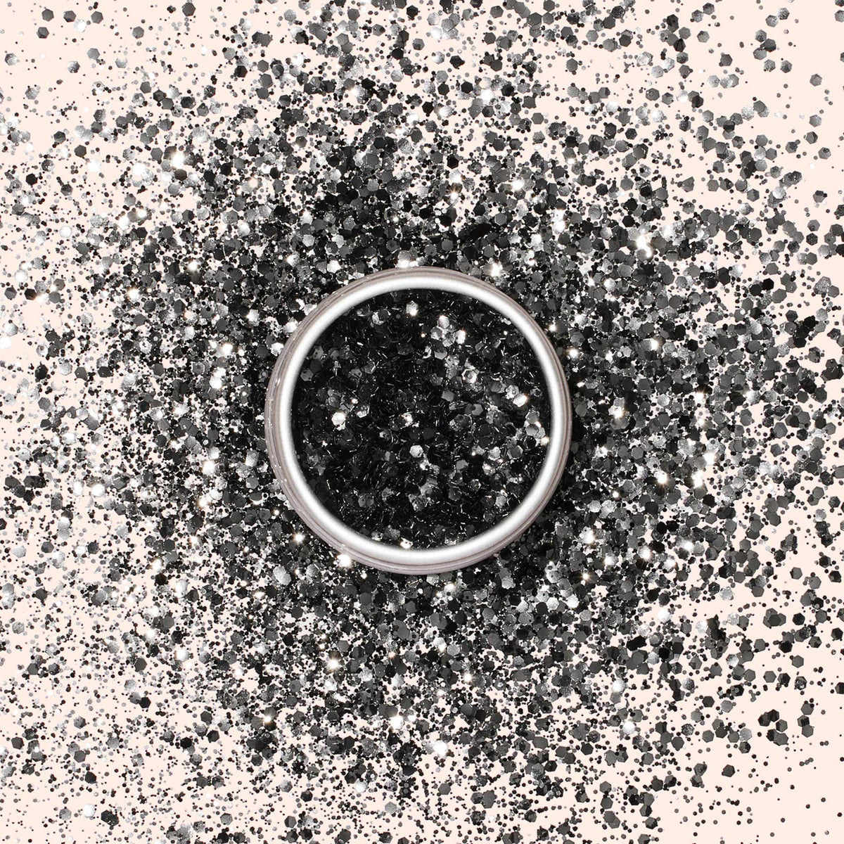 A silver ring sits atop a scattered pile of Manucurist Biodegradable glitter in black and silver hues on a light background.