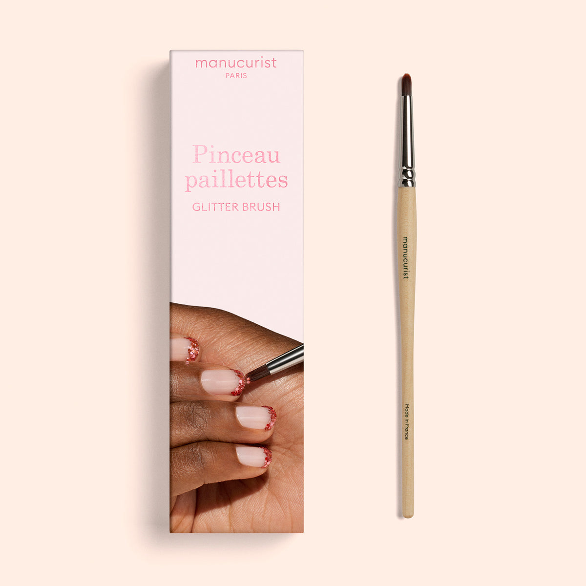 A box labeled Manucurist Glitter Brush sits beside a slim nail brush with a wooden handle and vegan synthetic bristles. The packaging features an image of a hand being decorated with glitter polish, highlighting the promise of a radiant manicure every time.