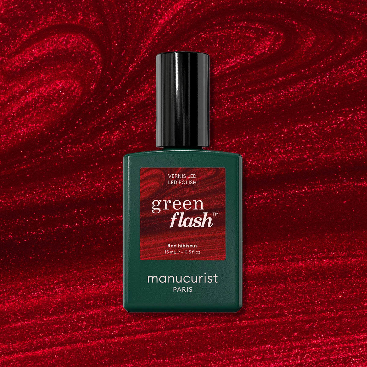 A bottle of Manucurist Red Hibiscus polish rests on a swirling, glossy red background that perfectly matches the vibrant shade of this Green Flash gel color.