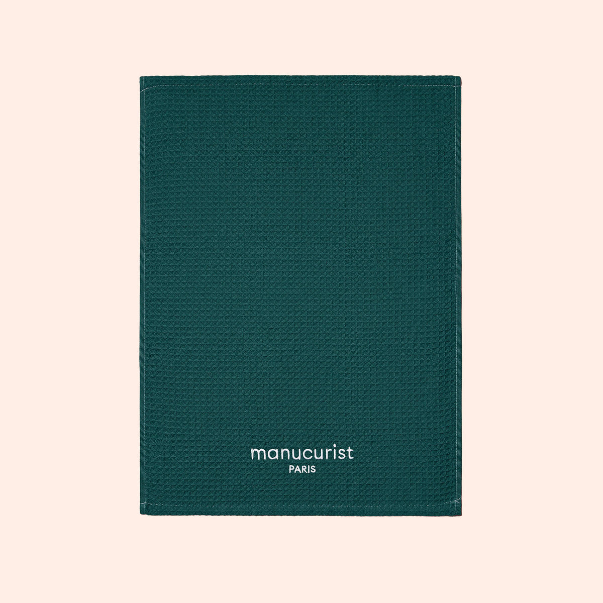 A textured dark green rectangular Manucurist notebook rests on a light beige background—ideal for manicure notes or pairing with your Manucurist Towel. "manucurist PARIS" appears in white at the bottom.
