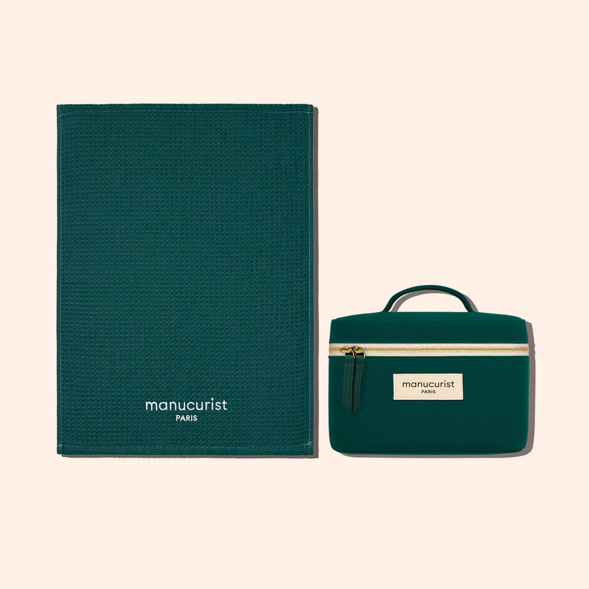 A dark green organic cotton Towel by Manucurist with a matching small zippered carrying case, both featuring Manucurist branding, displayed on a light beige background.