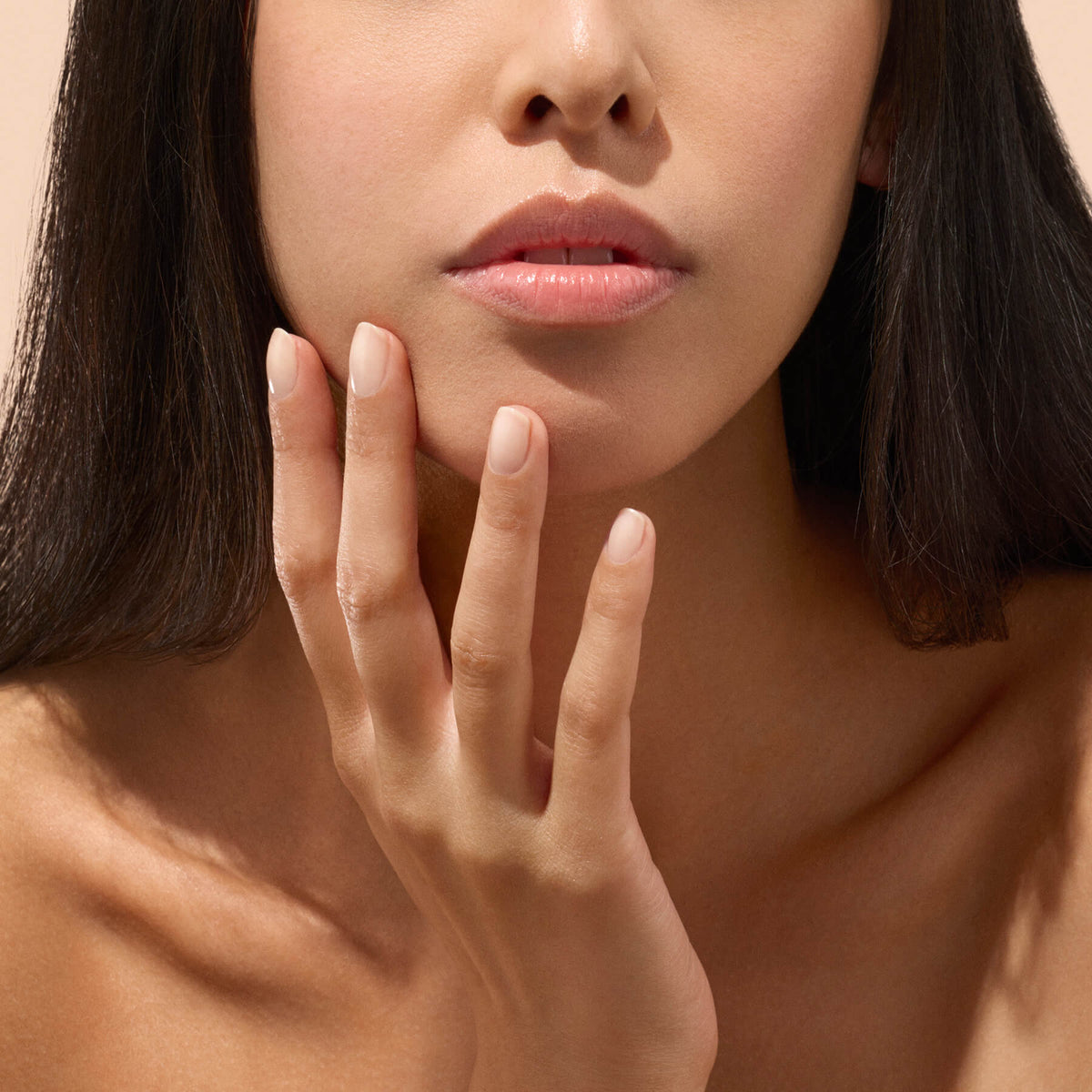 A woman with smooth skin gently touches her face with her hand, displaying well-groomed nails enhanced by Manucurist’s Active™ Smooth 01—a testament to her dedication to nail care. The image is cropped to highlight her lower face, lips, and fingers.