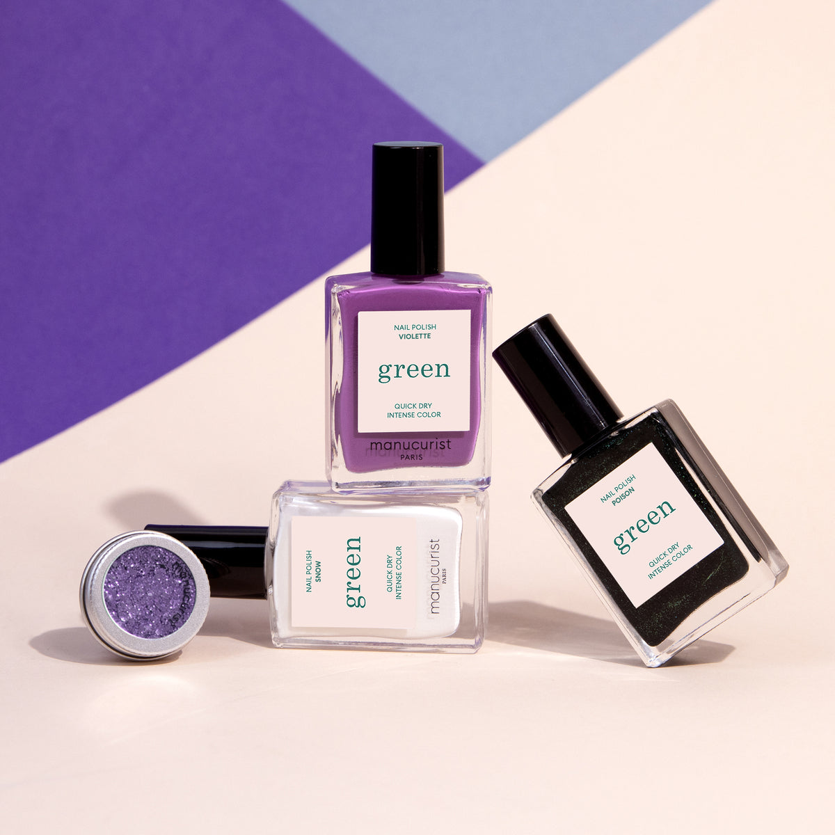The Witchy Wicked Set by Manucurist features four manicure essentials—a purple gel polish, clear and black nail polishes, and a small pot of biodegradable glitter powder—displayed on a pastel geometric background.