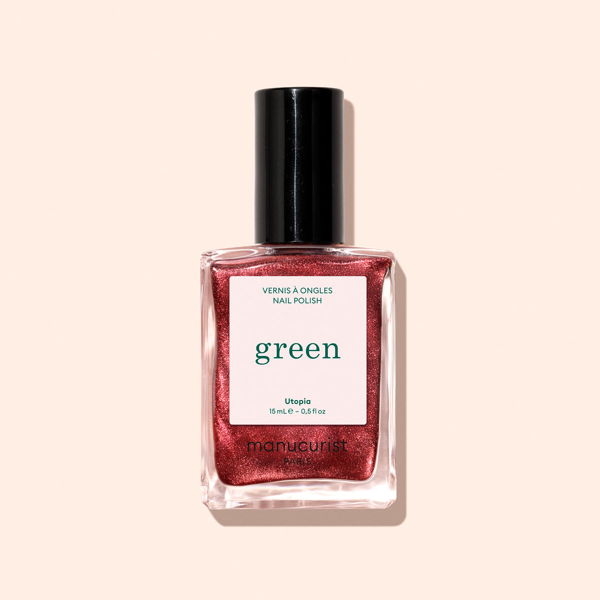 A bottle of Manucurist Green nail polish in the shimmery red Utopia shade with a black cap, shown against a light beige background.