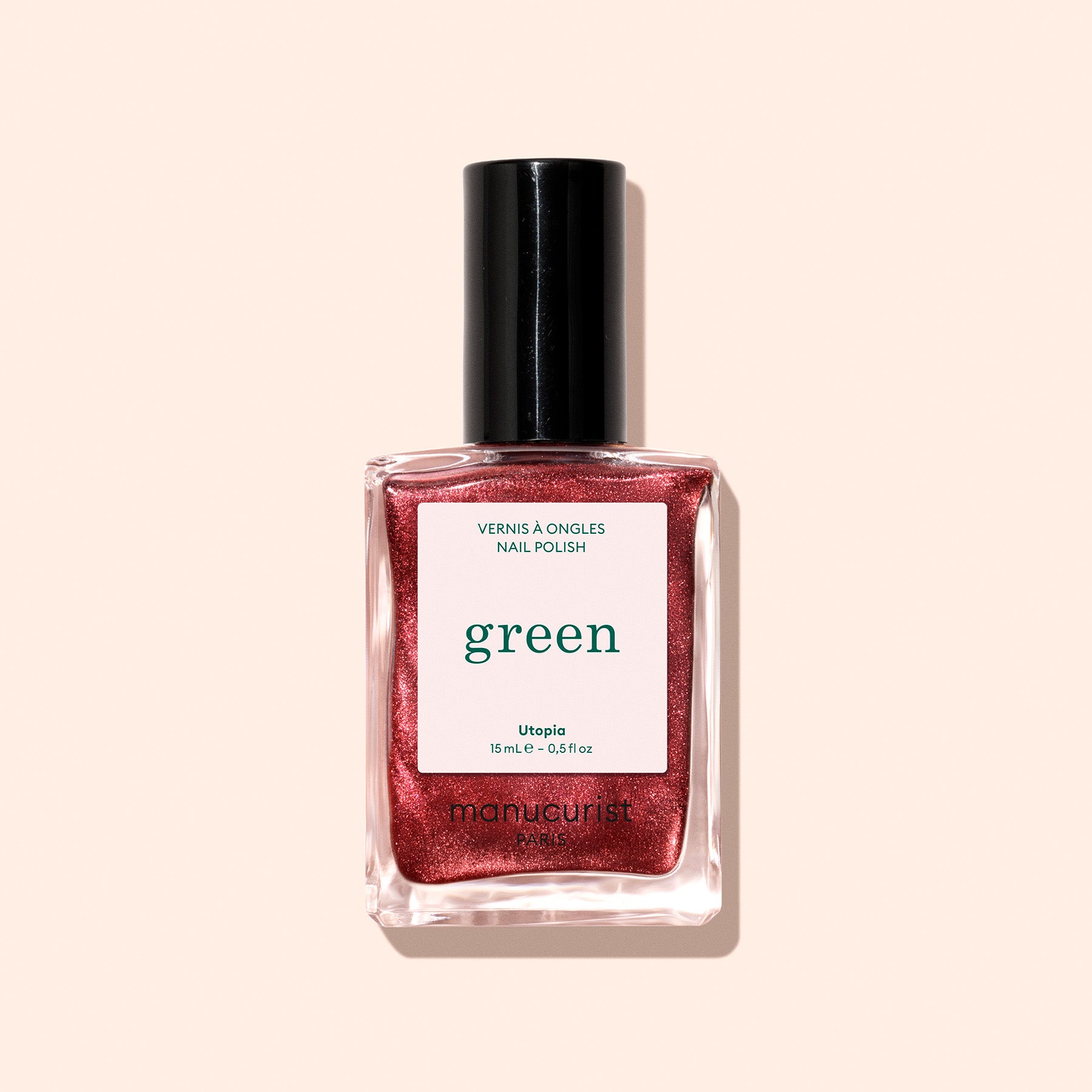 A bottle of Manucurist Green nail polish in the shimmery red Utopia shade with a black cap, shown against a light beige background.