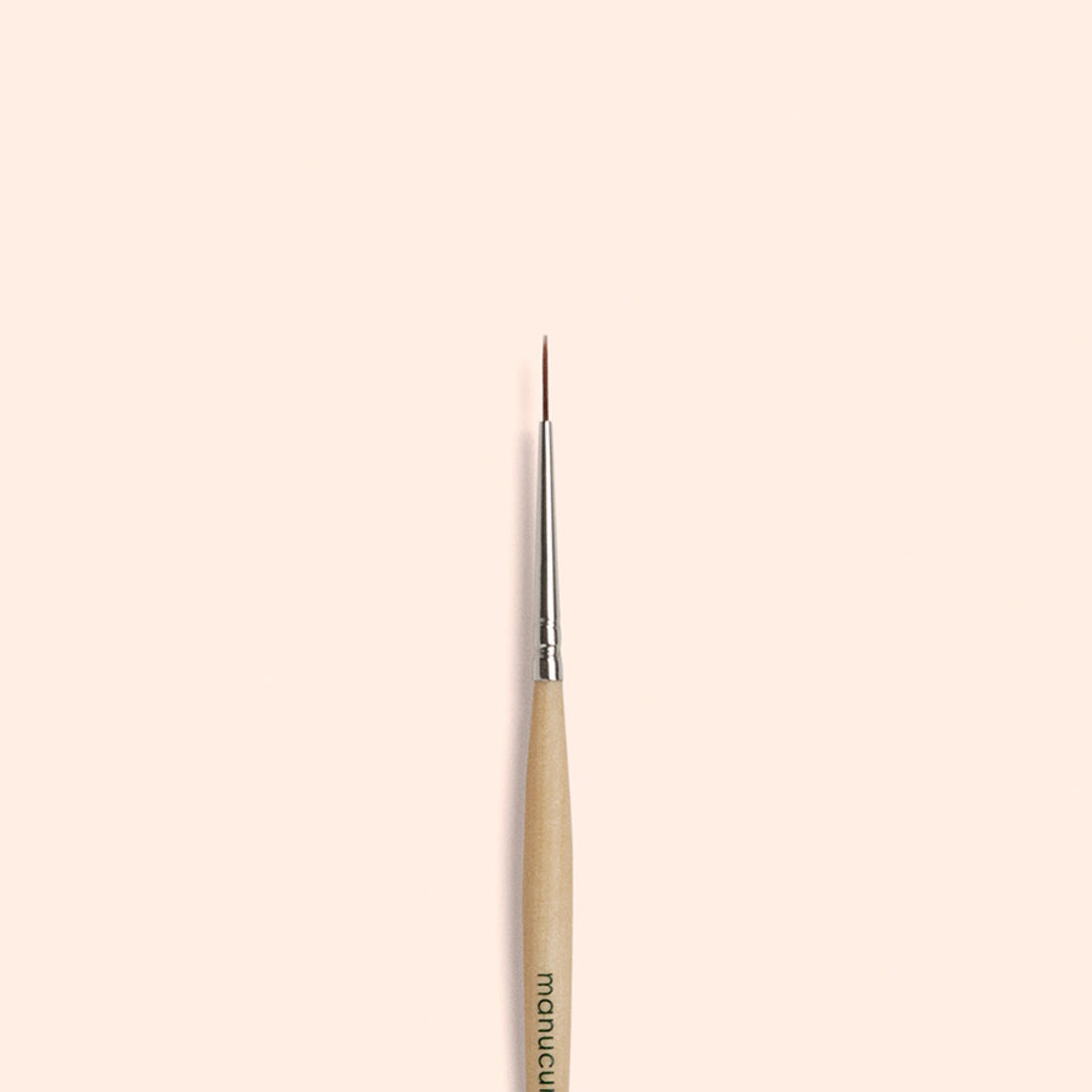 The Manucurist Liner Brush, featuring a thin, fine tip with a wooden handle and silver ferrule, is centered vertically on a plain beige background—perfect for creating precise nail art designs.