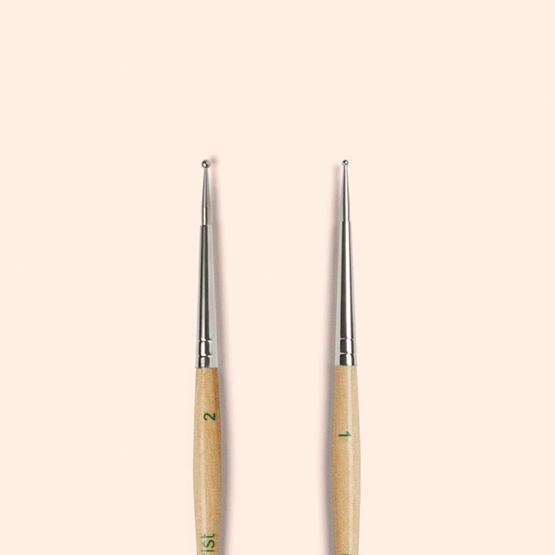 Two Manucurist Dotting Tools with metal tips and wooden handles stand upright side by side on a beige background—ideal for precise nail art designs in your tool collection.