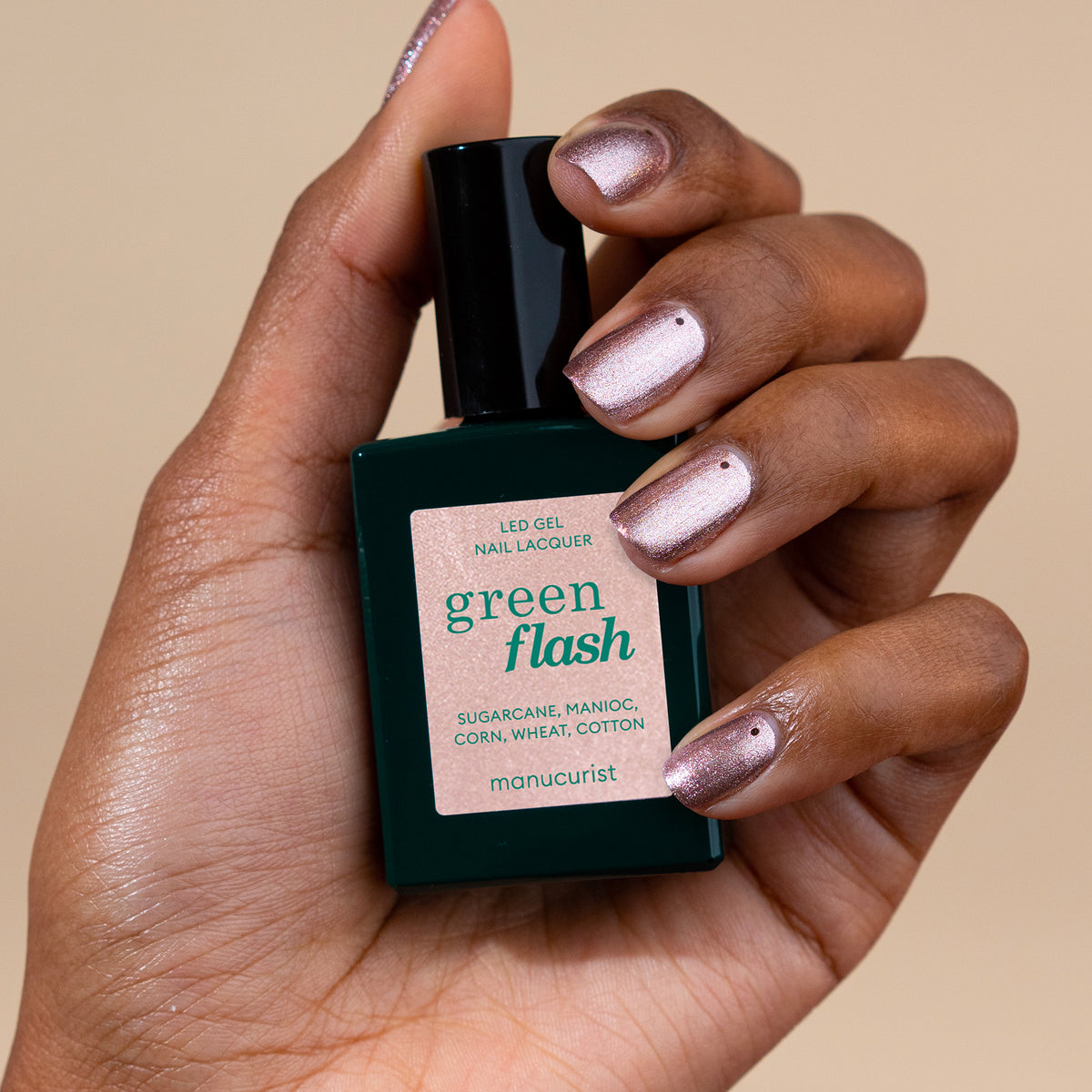 A hand with iridescent pink polish holds a green bottle of Manucurist&