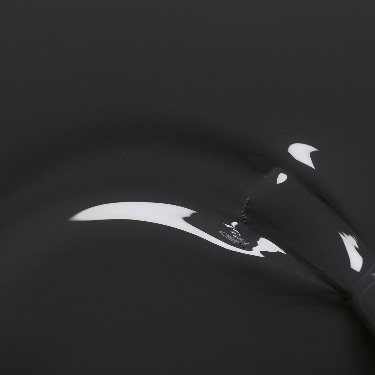 A close-up of glossy black liquid recalls the sleek finish of Manucurist’s Anthracite nail polish, as smooth curves and bright reflections evoke an abstract, minimalist style.