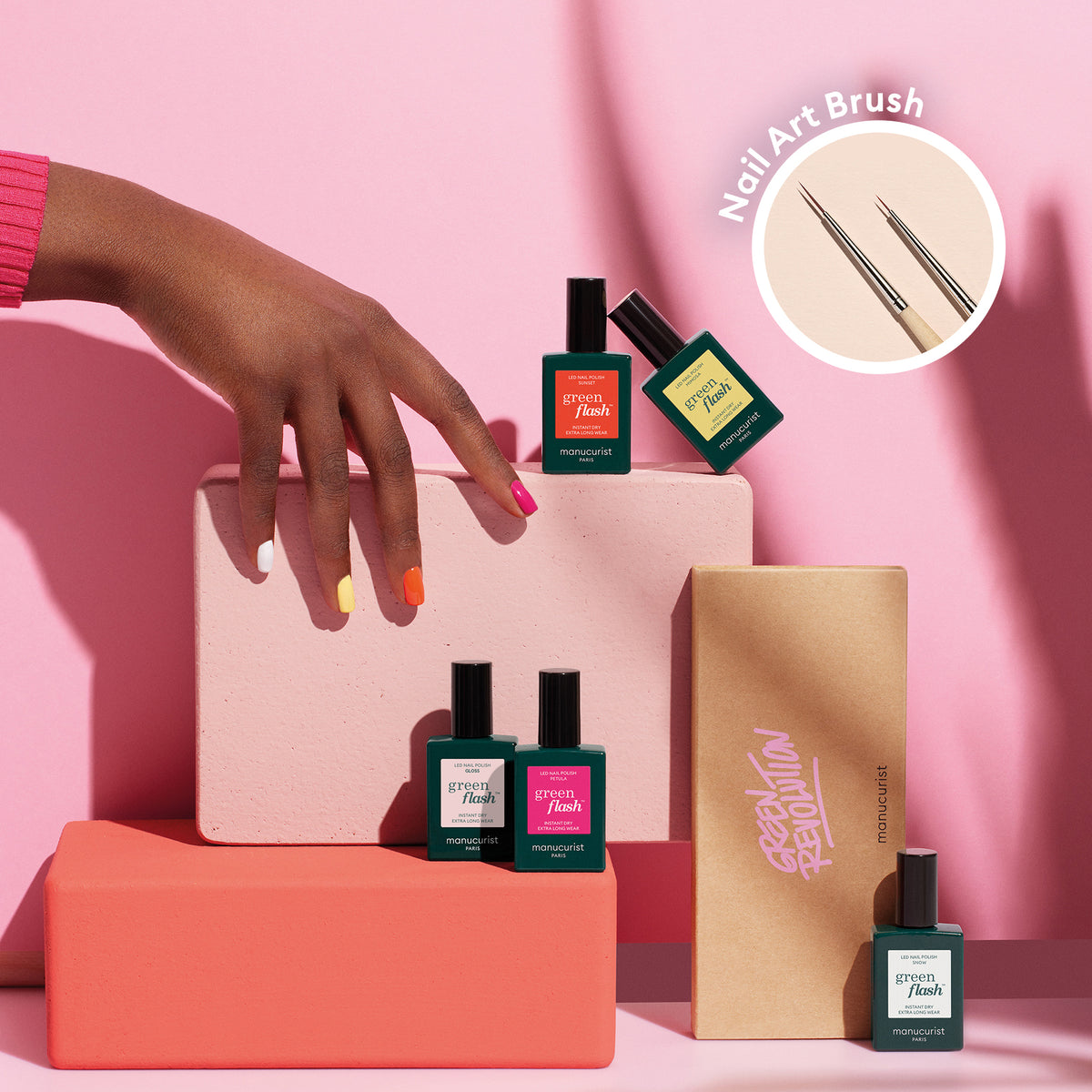 A hand with colorful, multi-shade painted nails from Manucurist’s Smile! collection rests on pink and beige blocks, surrounded by four nail polish bottles and an open Nail Art Liner Brush box. Inset shows two thin brushes—perfect for summer nail art.