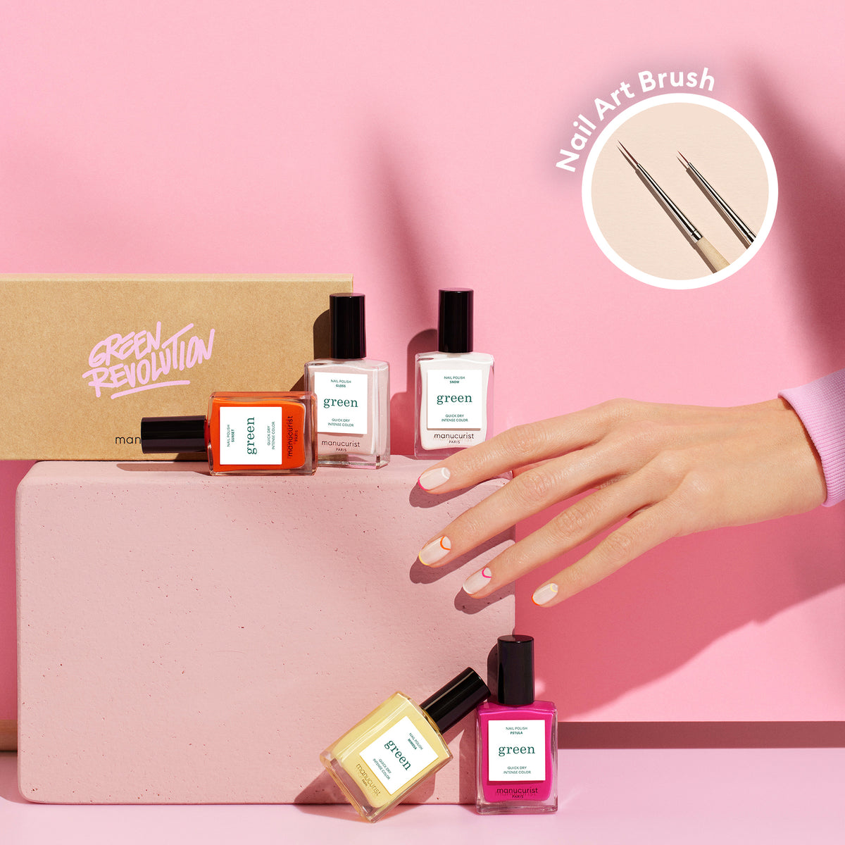 A hand with pastel-colored Smile! nails from Manucurist rests on a pink block, surrounded by vibrant summer polishes. A Green Revolution box and an inset of the Nail Art Liner Brush complete the scene.