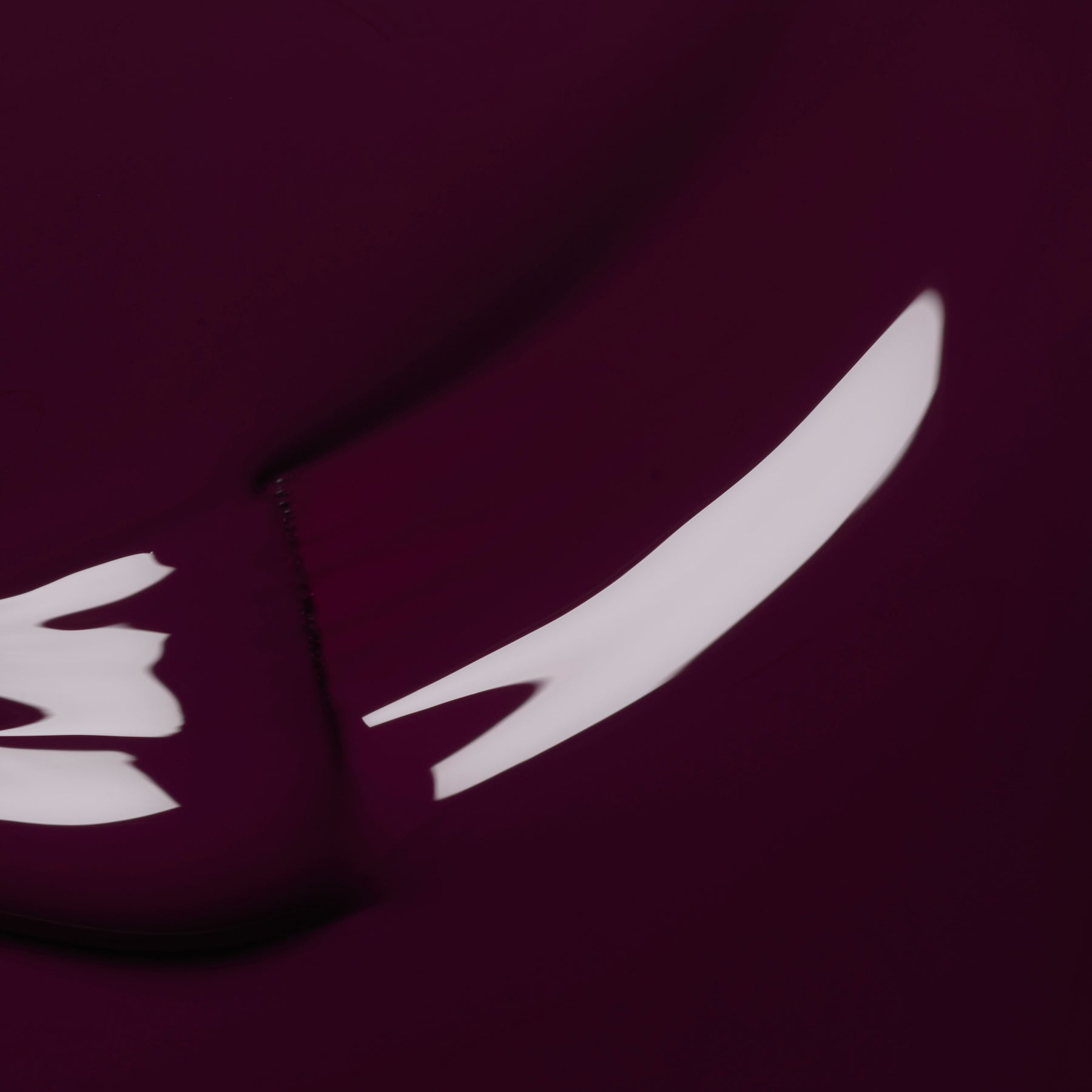 An abstract image with a deep maroon background and white, curved streaks—evoking the smooth, fluid look of Manucurist’s Aubergine gel polish—creates dynamic motion across the canvas.