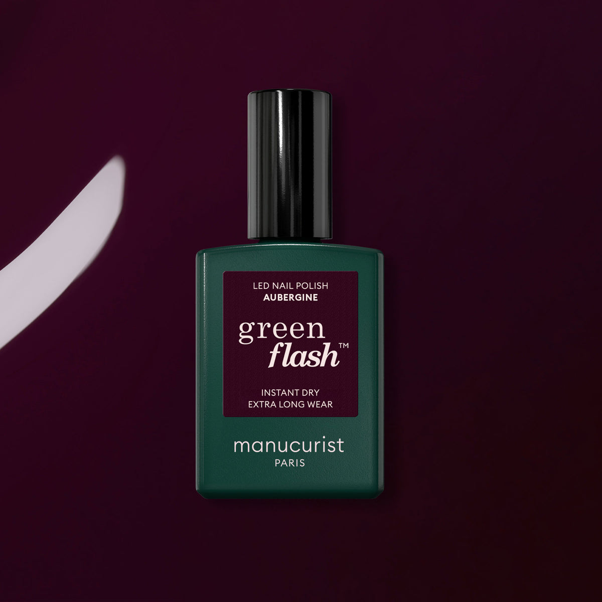 A bottle of Manucurist Aubergine gel polish sits on a dark purple surface, with a matching brushstroke of this rich shade displayed beside it.