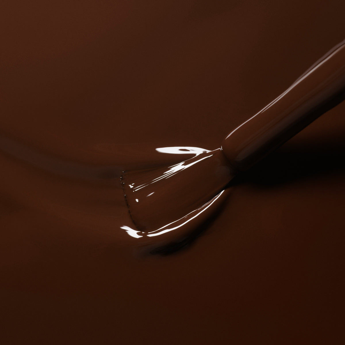 A close-up of a brush dipped in Manucurist’s Clove, a rich chocolate brown gel polish, ready for flawless application.