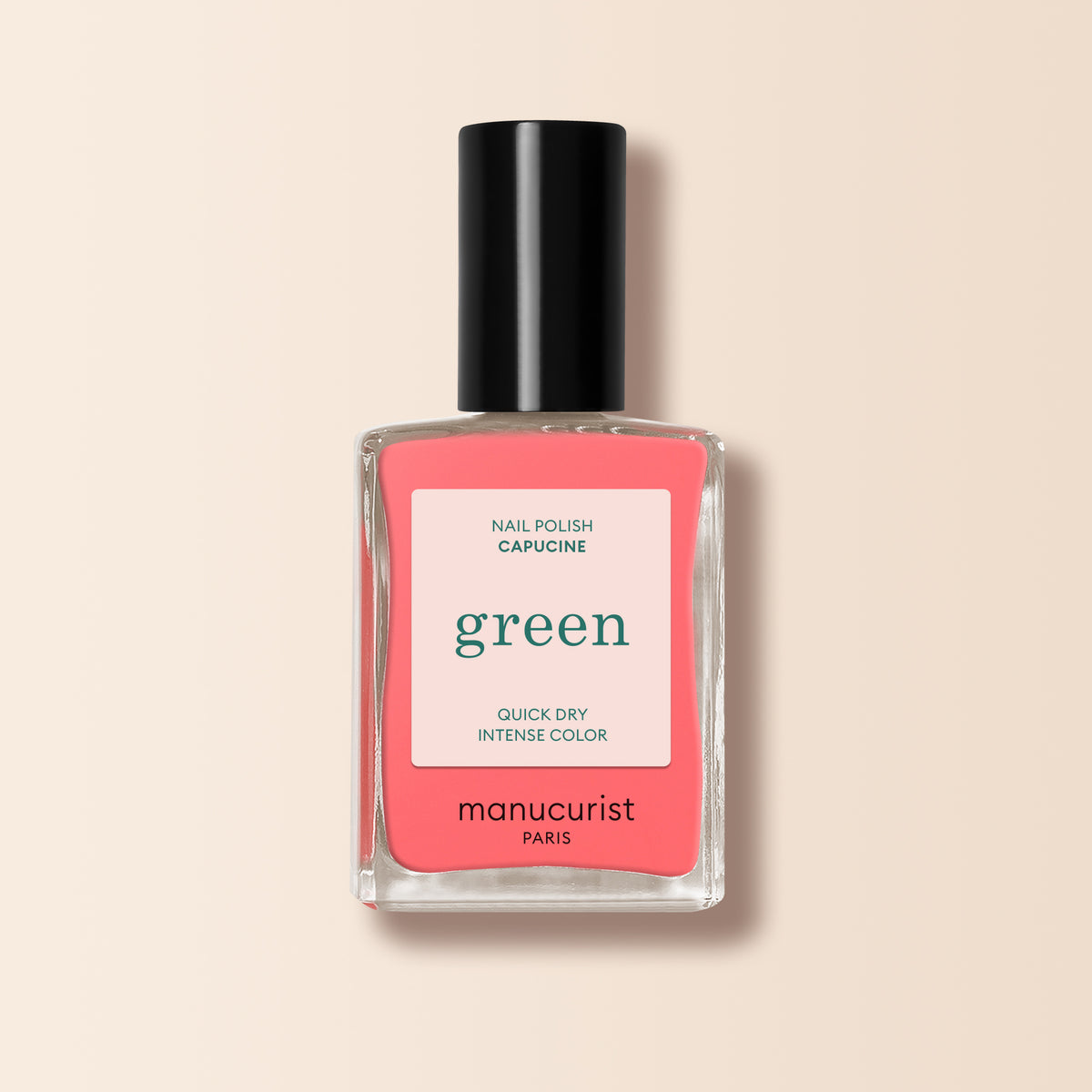 A bottle of Manucurist Capucine nail polish from the Green range, featuring a coral pink shade and a black cap, is shown on a light beige background.