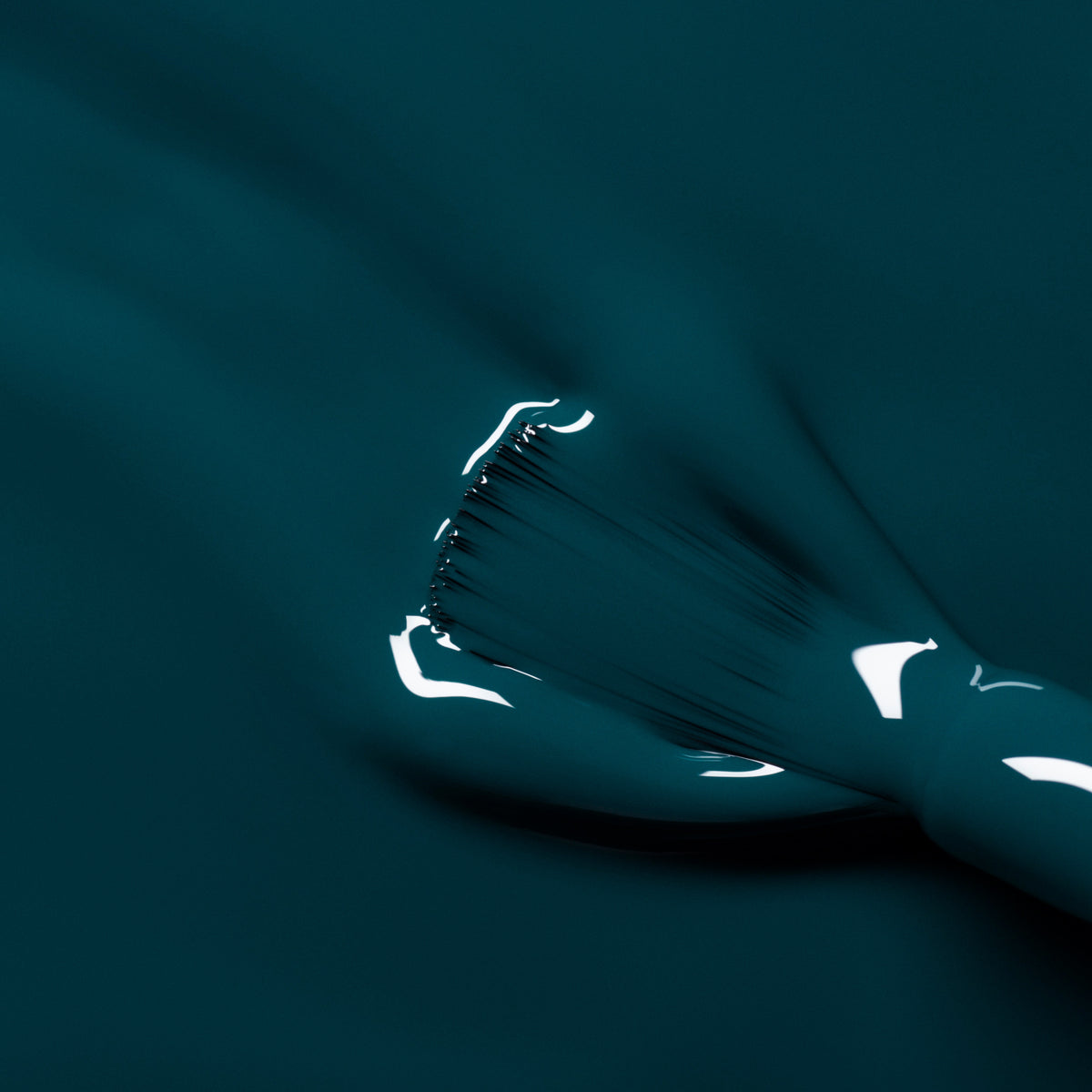 A close-up of a brush applying Manucurist’s "Dark Clover" nail polish, creating smooth, glossy teal-green strokes across the surface.