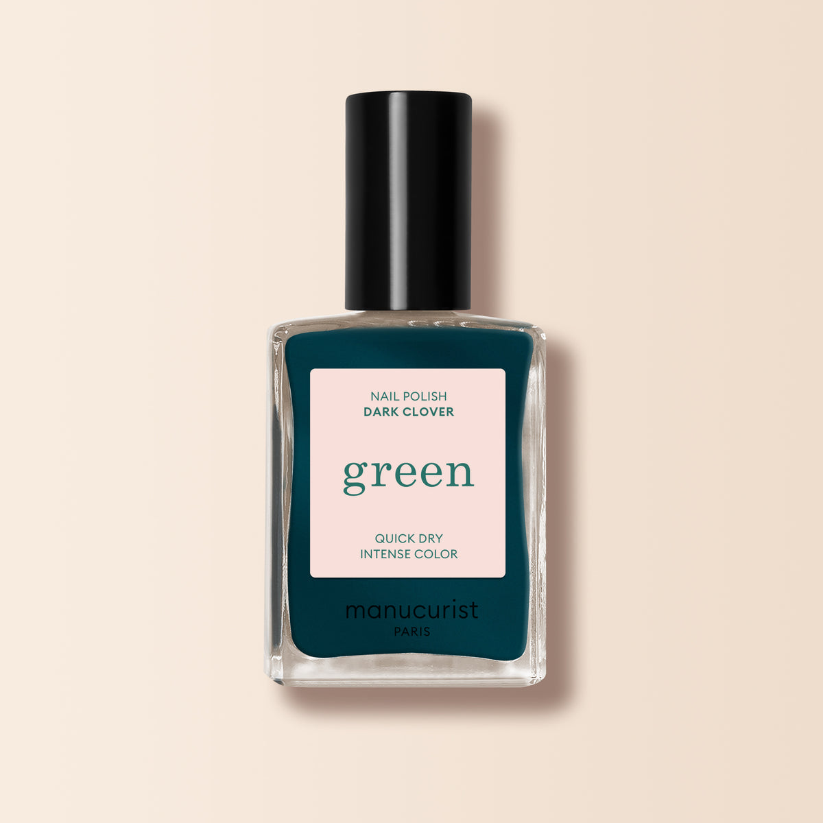 A bottle of Manucurist Dark Clover nail polish, a dark green-teal shade from the Green range, with a black cap and beige label, is displayed on a soft beige background.