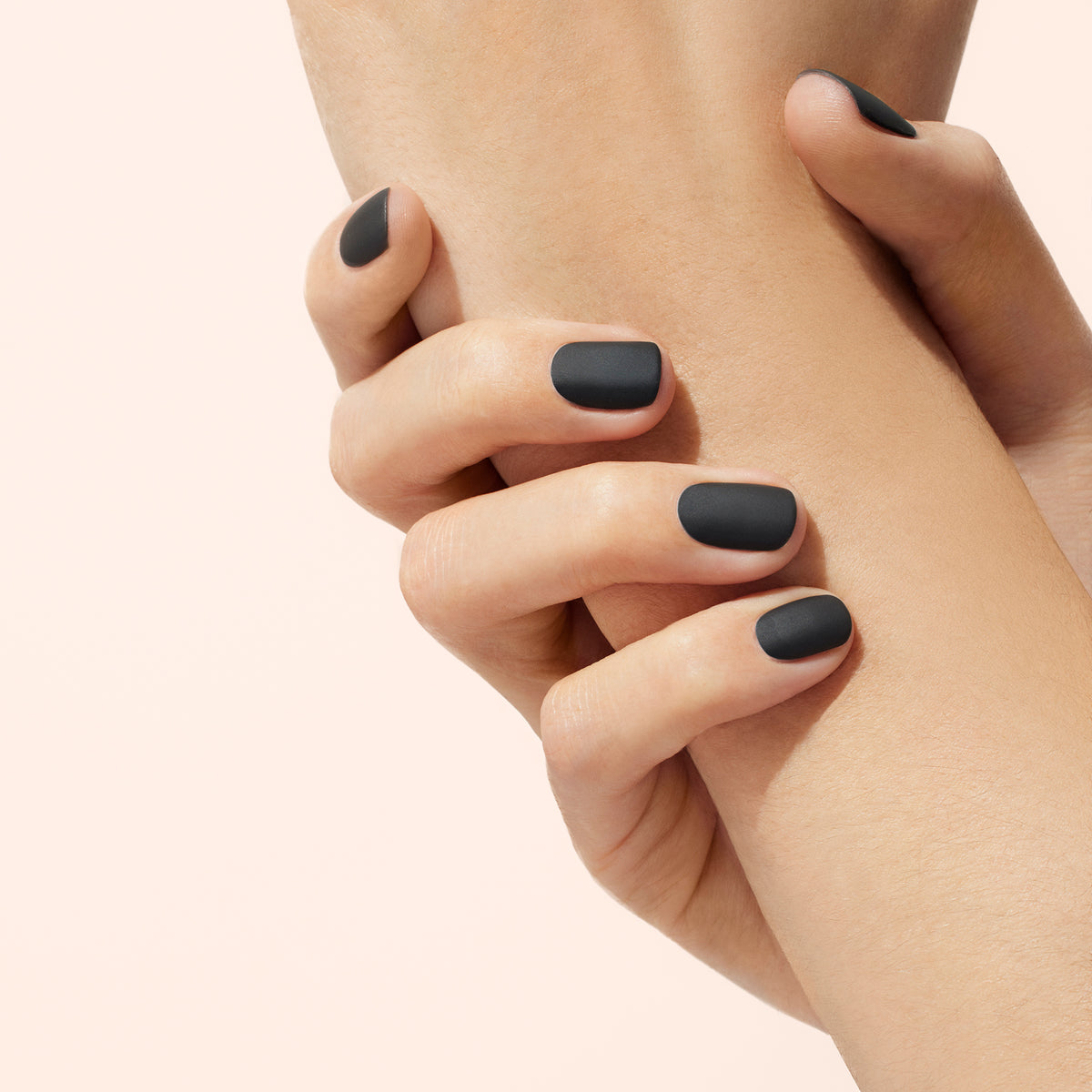 A close-up of a hand gently holding a wrist, both with neatly manicured nails finished with Manucurist Matte Top Coat, set against a soft beige background.