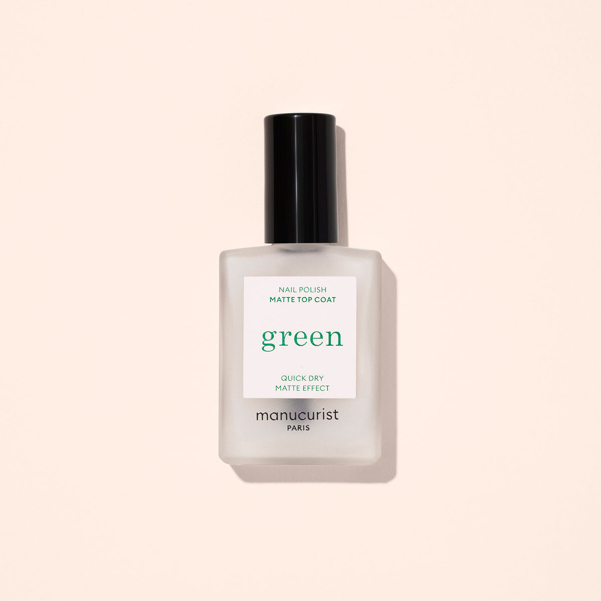 A frosted glass bottle of Manucurist Matte Top Coat nail polish with a black cap sits against a light beige background, featuring a label that highlights its quick dry and matte effect.