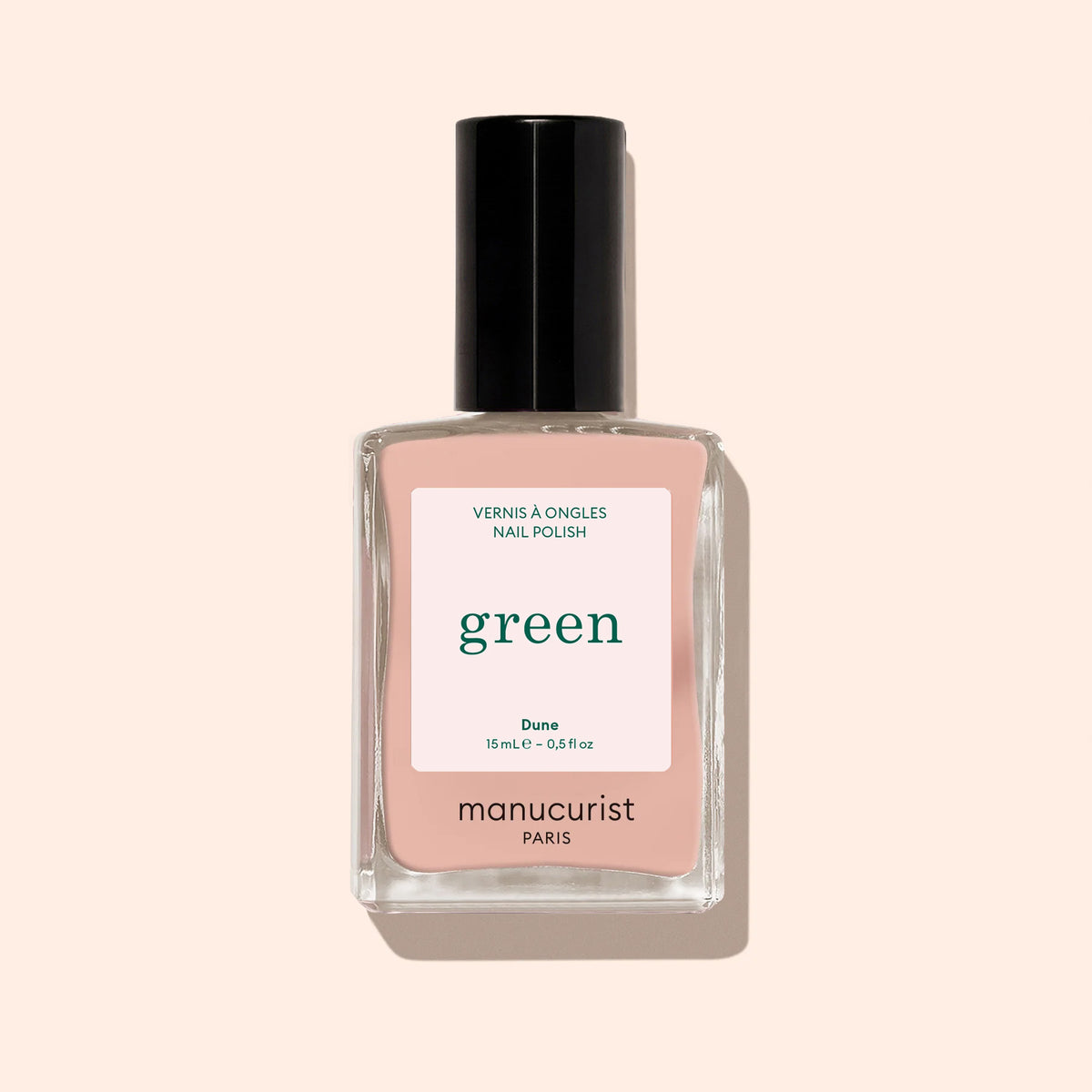 A bottle of Manucurist nail polish in the shade Dune, a beige-pink hue with orange undertones, featuring a black cap and minimalist label on a soft beige background.