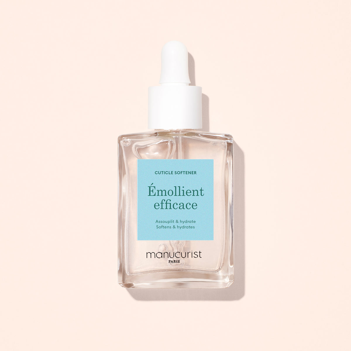 A clear glass dropper bottle labeled "Cuticle Remover Pusher Duo" by Manucurist, with a white cap and light blue label, ideal for nail care and gentle cuticle removal, set against a pale pink background.
