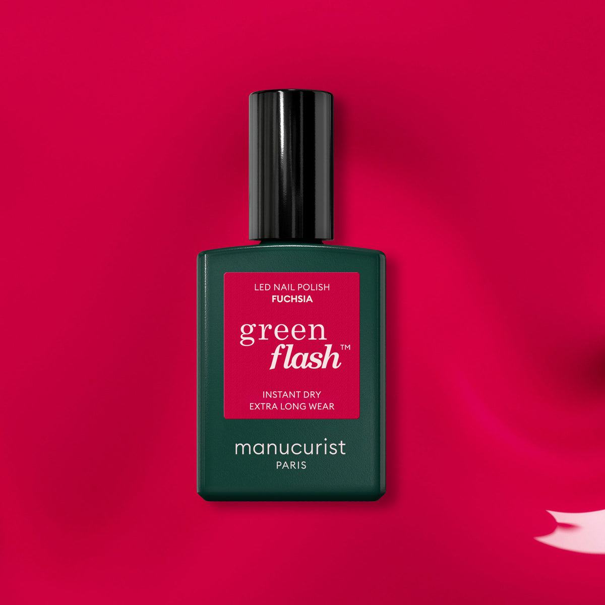 A bottle of Manucurist Fuchsia Green Flash gel polish sits against a vibrant pink backdrop with a highlighted swirl effect.