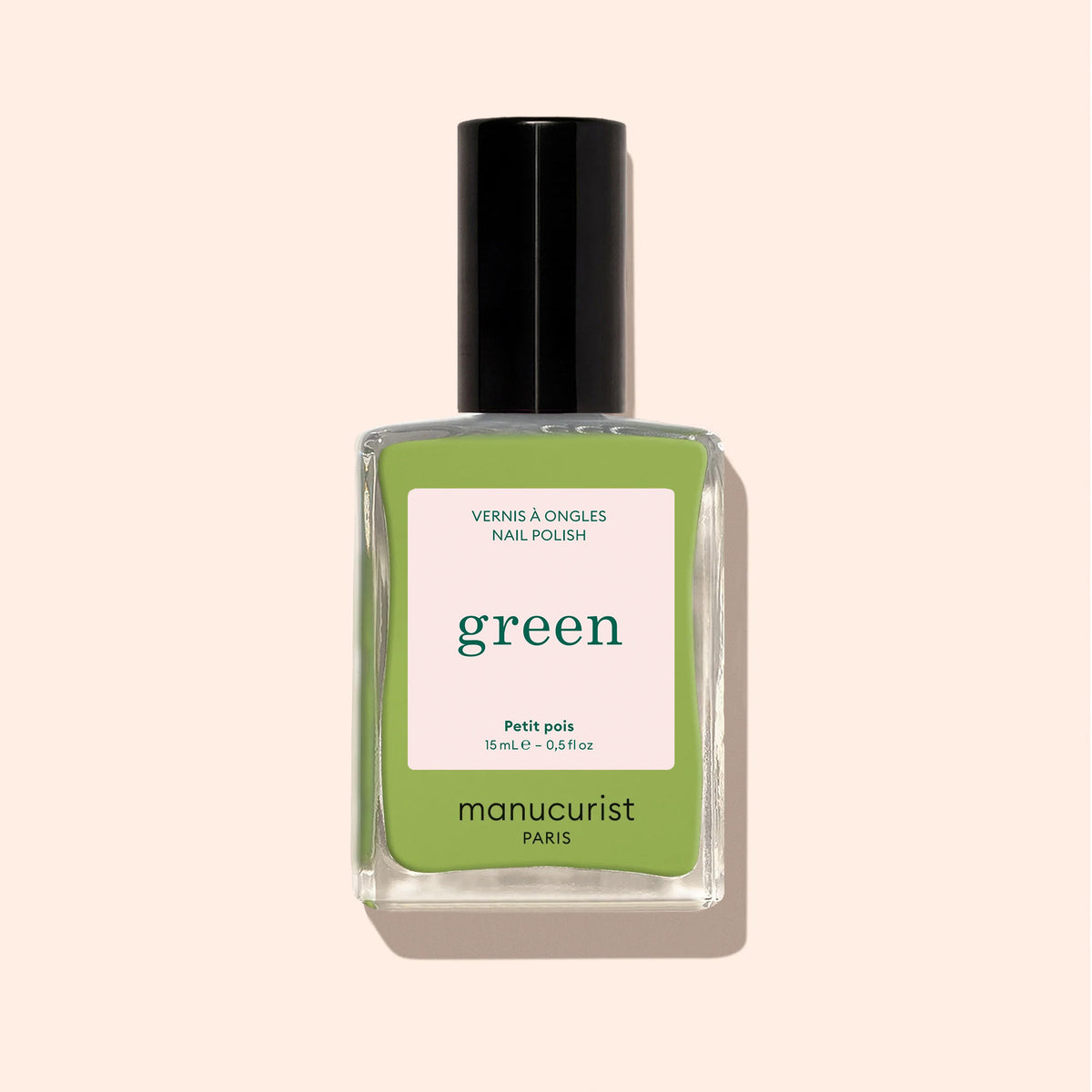 A bottle of Manucurist Sweet Pea nail polish from the Green range, featuring a black cap and quick-dry intense color, adds a vibrant touch against a light beige background.