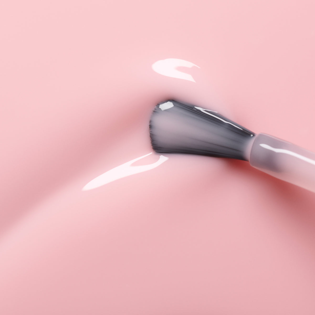 A close-up of the Manucurist Hortencia brush applying sheer pink gel polish, creating glossy streaks that reflect light on a smooth surface.