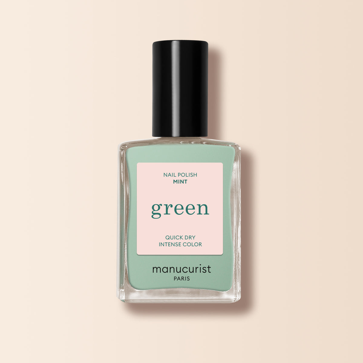 A bottle of Manucurist Mint nail polish from the Green™ range, in a delicate pastel green shade with quick-dry intense color. It features a black cap and pale pink label, shown on a pale beige background.