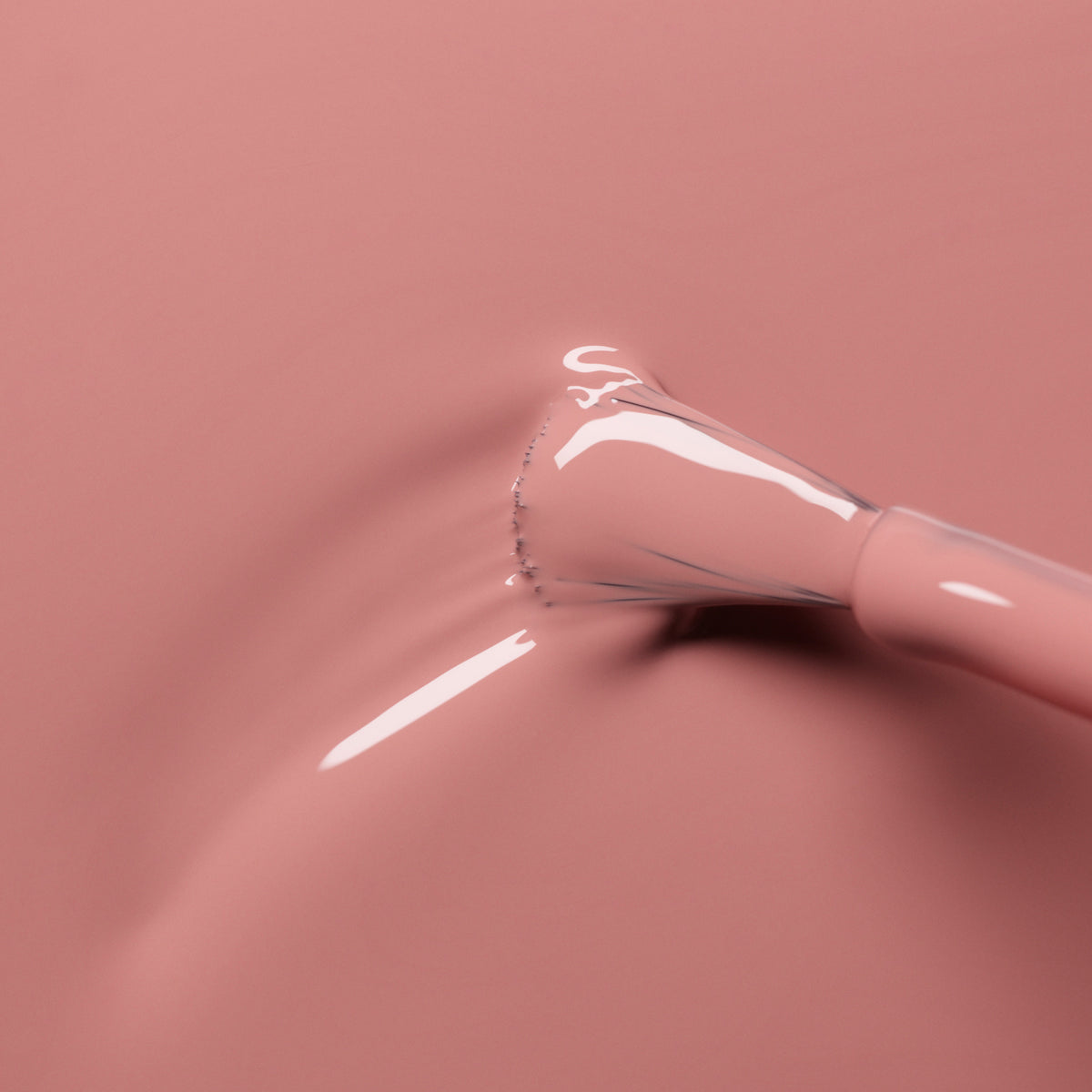 A close-up of a Manucurist Old Rose nail polish brush sweeping through glossy, powder pink gel, creating subtle ripples on the smooth surface.