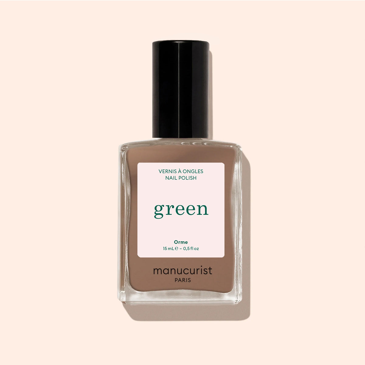 A bottle of Manucurist Orme nail polish from the Green range rests on a beige background, displaying its chic café au lait shade and stylish taupe-brown color. The label highlights: Orme, Green, Quick Dry, Intense Color.
