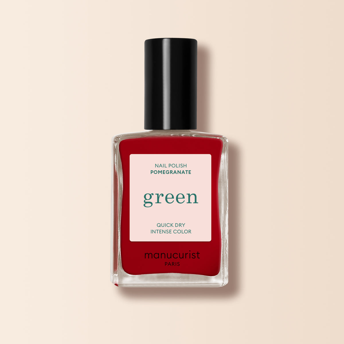 A bottle of Manucurist Pomegranate nail polish from the Green range, featuring a black cap and white label, is shown on a light beige background.