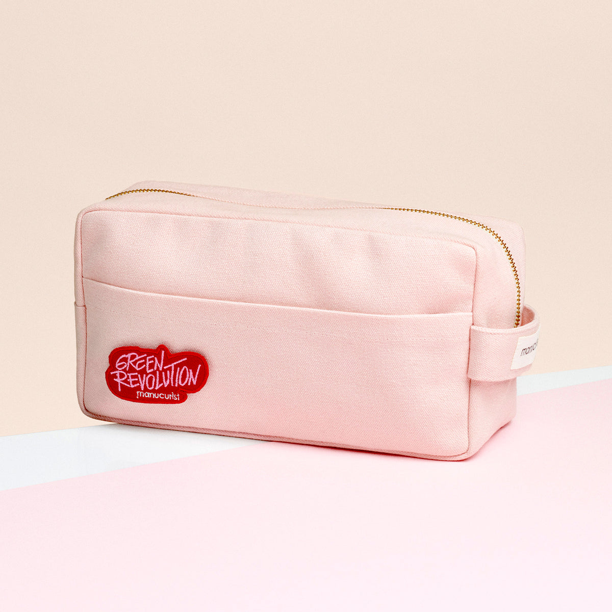The Pink Pouch by Manucurist is a light pink rectangular organic cotton pouch with a zipper, front pocket, and small handle. It has a red patch reading GREEN REVOLUTION and Mancusi, perfect as a chic makeup organizer or storage pouch.