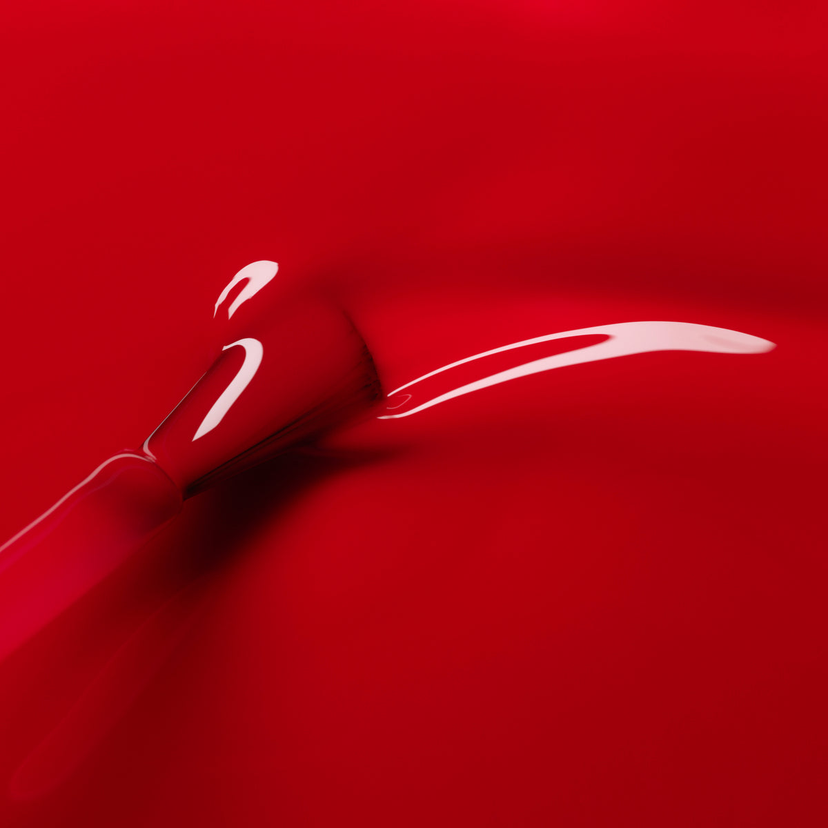 A close-up of a brush applying Anémone by Manucurist, a juicy red glossy nail polish, on a matching red surface with a visible wet streak and light reflecting off its shiny finish.