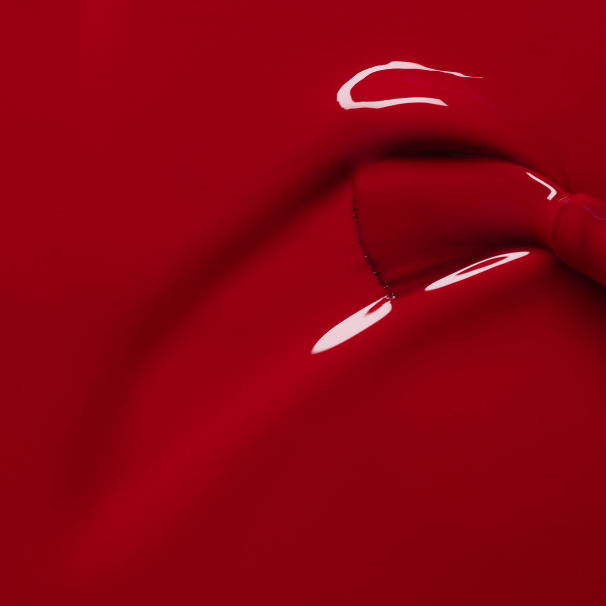 A close-up shows Manucurist’s Dark Dahlia nail polish being brushed on, with visible brushstrokes and reflections that highlight its deep red, shiny texture.