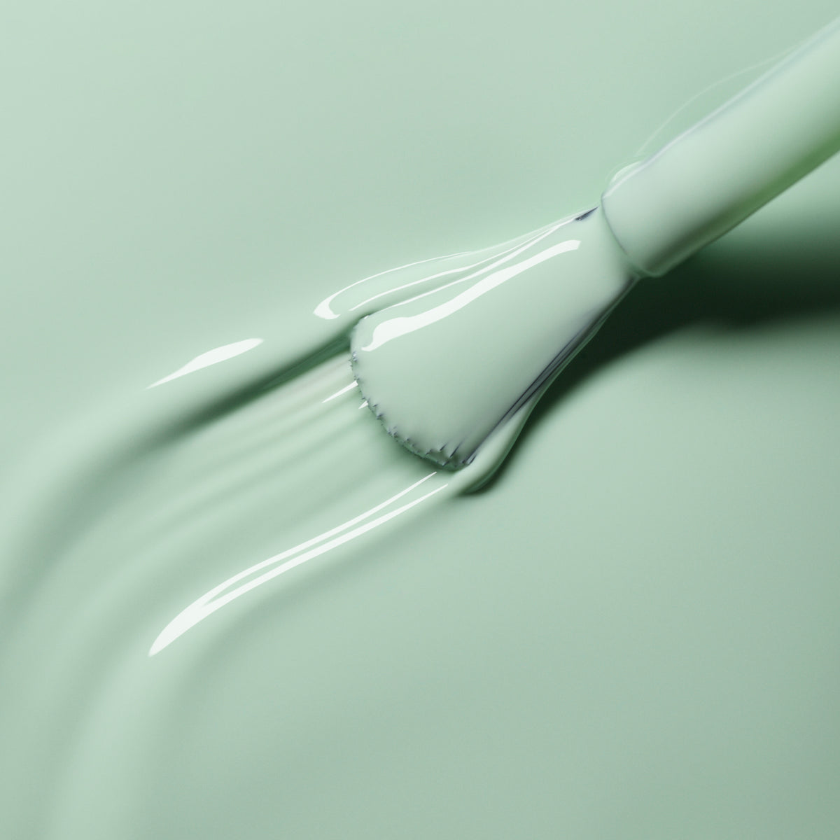A close-up shows a brush applying Manucurist Mint, a pastel green nail polish, onto a matching light green surface. The smooth, creamy texture and glossy finish are highlighted in the brush strokes.