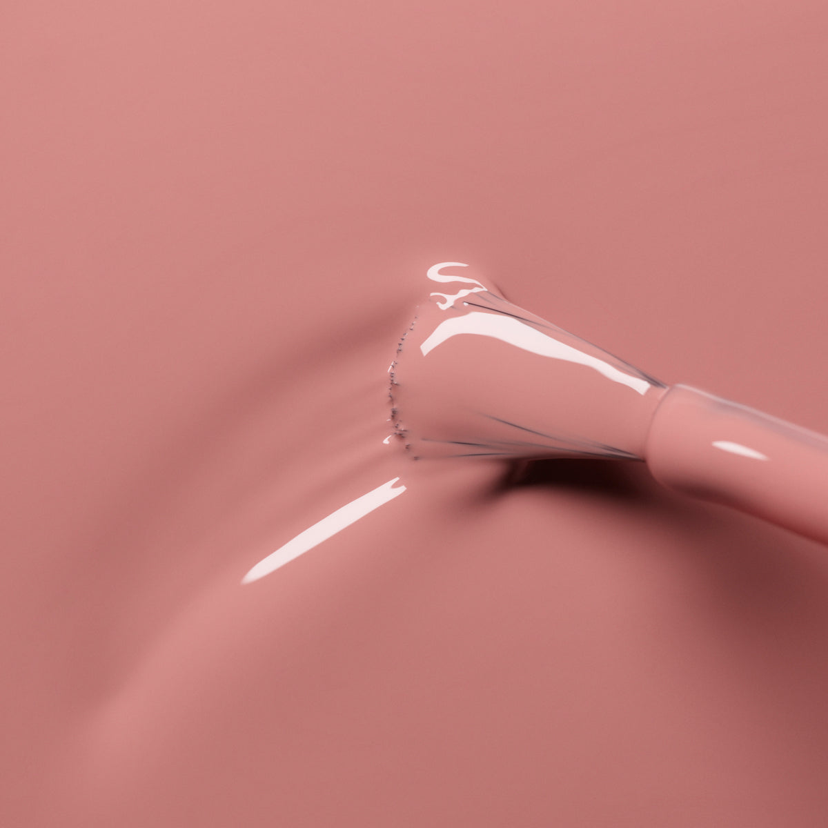 A close-up of a brush applying Manucurist Old Rose glossy nail polish, an antique powder pink shade from the Green™ range, with smooth ripples visible in the liquid.