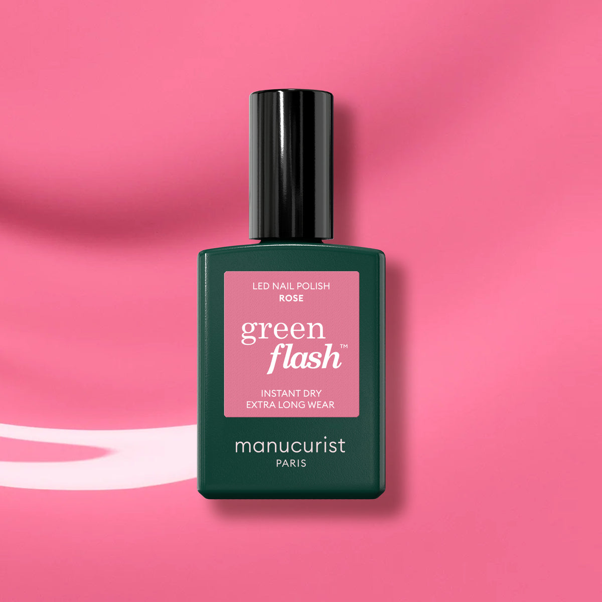 A bottle of Manucurist Rose Green Flash gel polish, featuring a dark green cap and label, is set against a pink wavy background.
