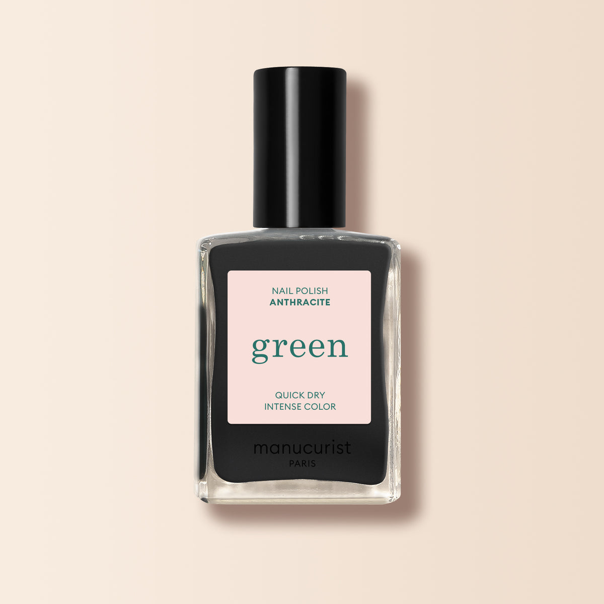 A bottle of Manucurist nail polish in the shade "Anthracite," a dark grey from their Green™ range, features a black cap and a square glass bottle with a light pink label, shown on a beige background.