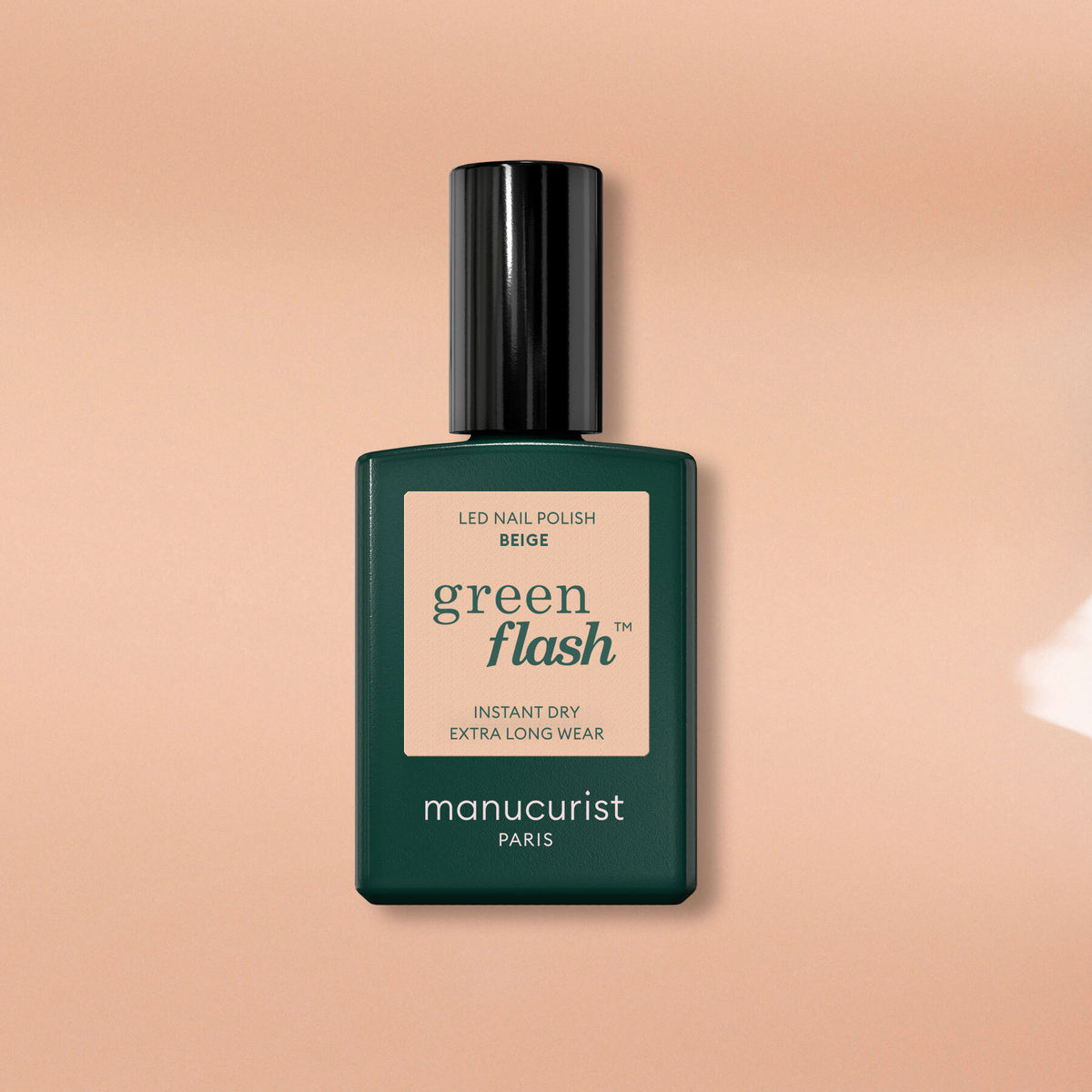 A bottle of Manucurist Beige nail polish with a dark green rectangular cap is placed on a pale beige surface.