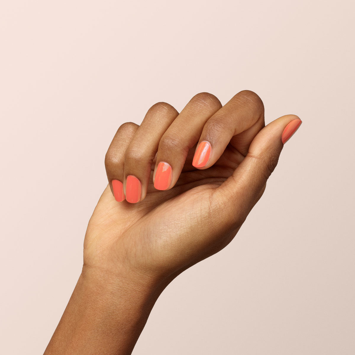A hand with medium brown skin is shown against a light beige background, featuring neatly manicured nails painted with Manucurist&